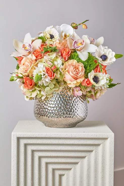 Mixed bouquet of peach and white flowers in a silver vase