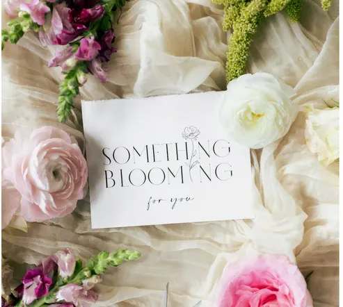 Floral arrangement with pink and white blooms around a card reading "Something Blooming for you"
