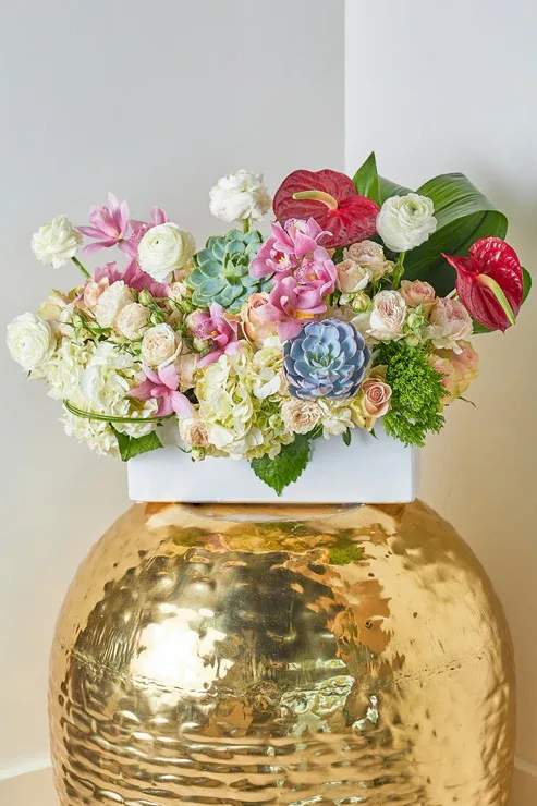 Mixed floral arrangement in a white container on a gold vase