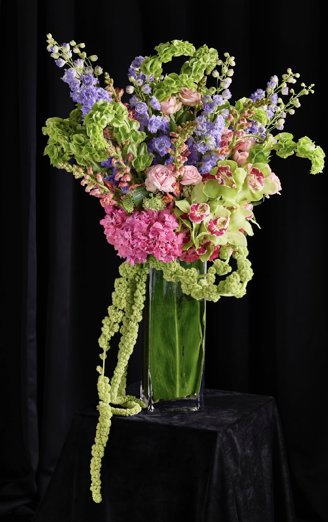 Tall mixed floral arrangement in a clear glass vase with pink, purple, and green blooms