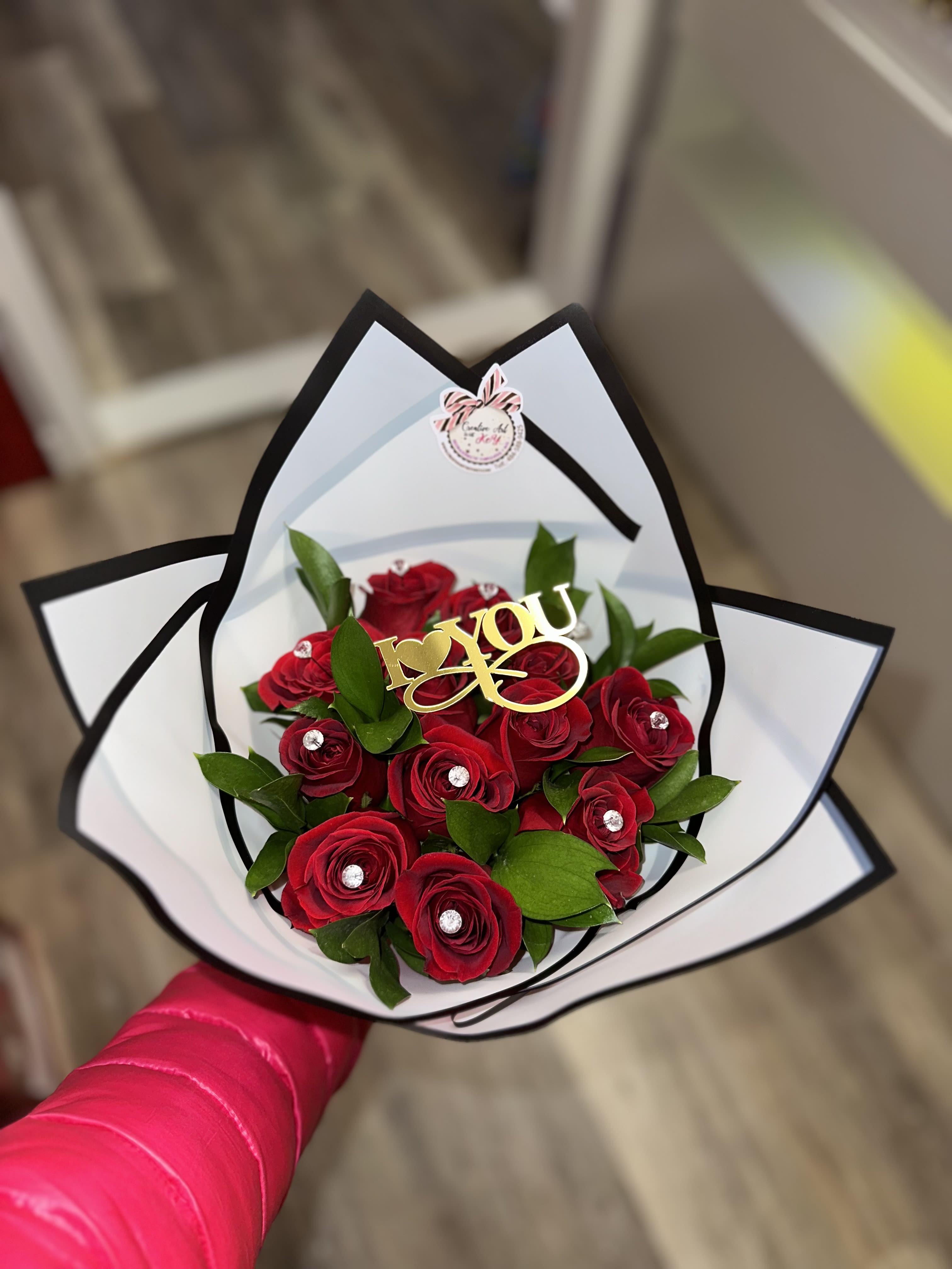 Red roses arranged in a white and black wrapped bouquet with a gold "I love you" topper