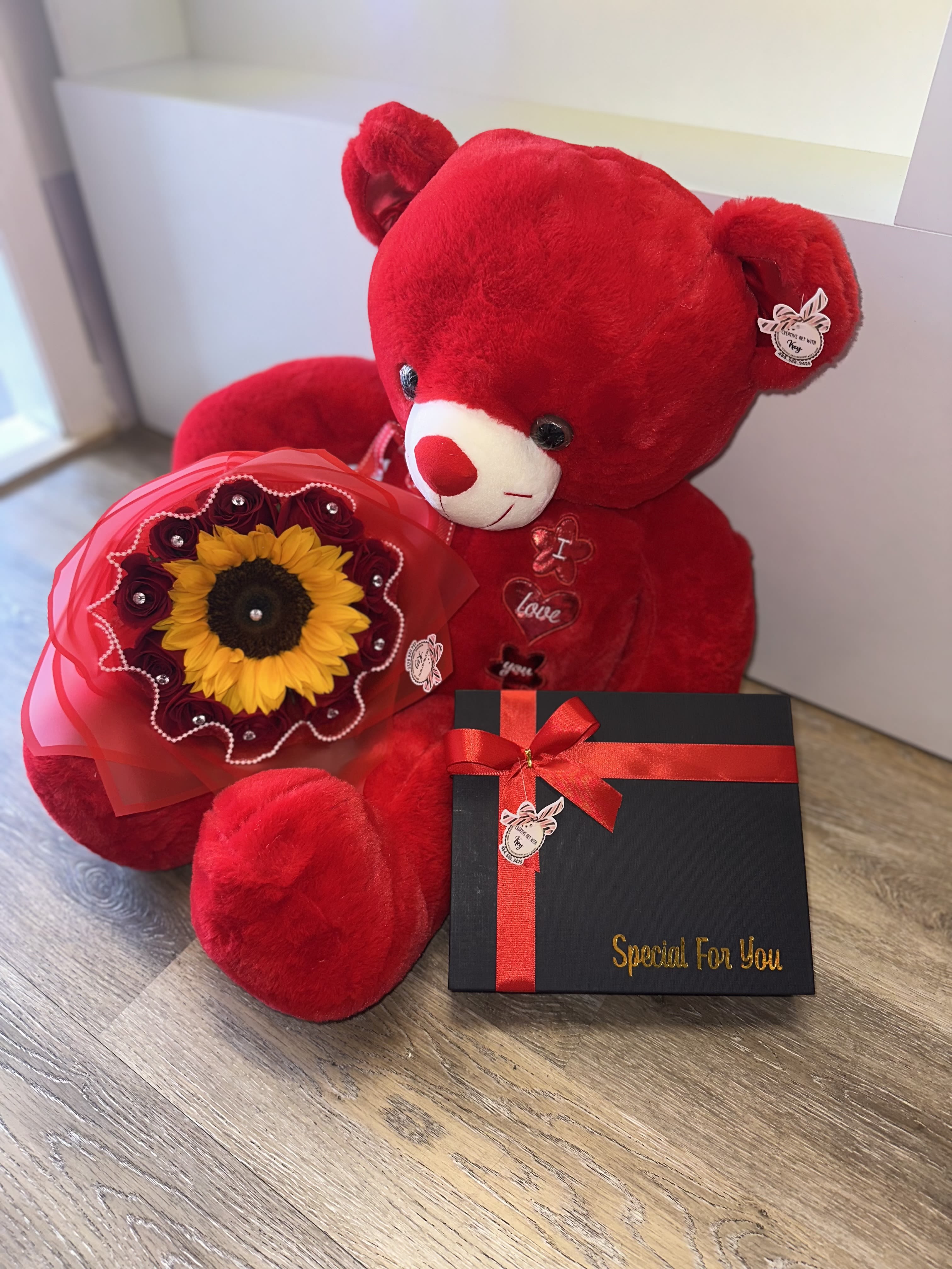 Red teddy bear with a sunflower bouquet and a black gift box with ribbon