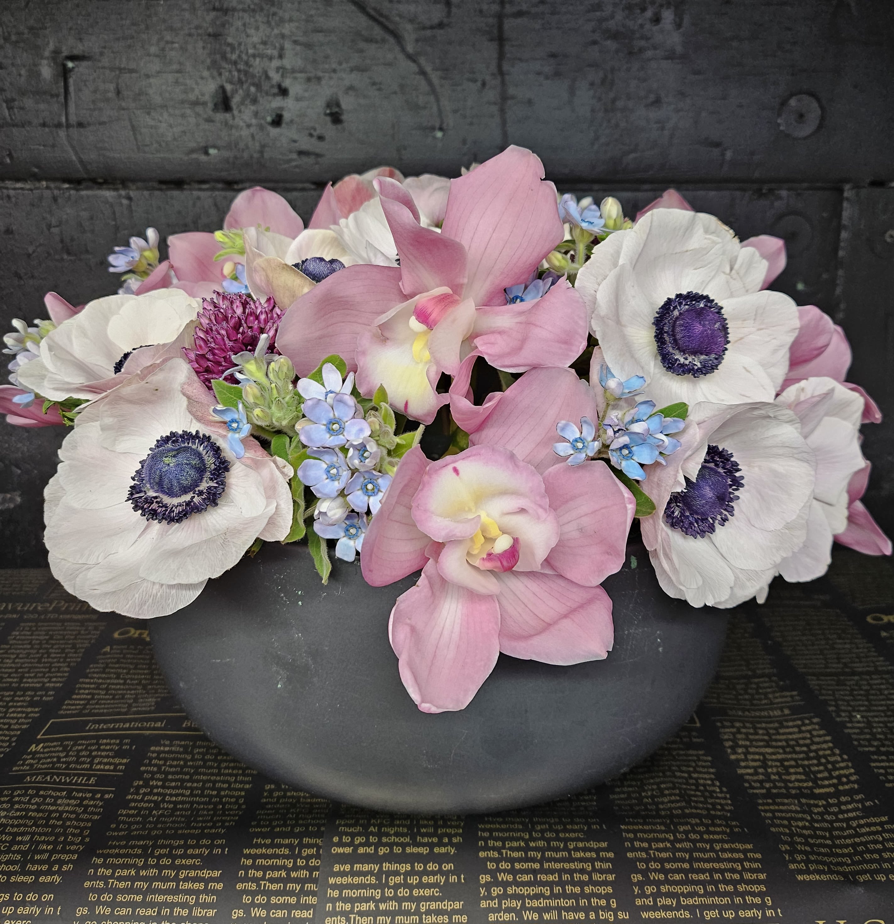 Pink orchids and white anemones arranged in a dark bowl