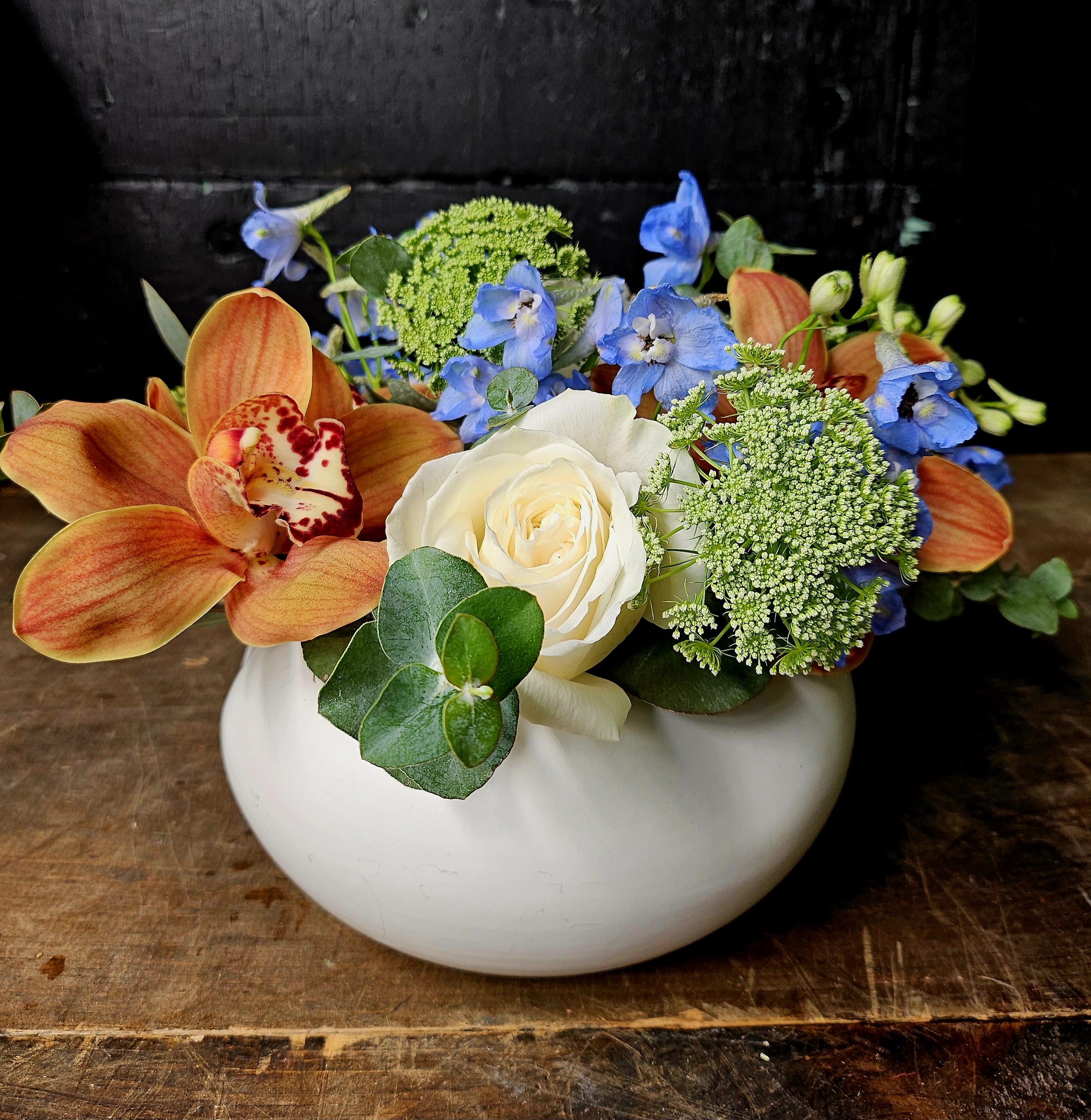 Orange orchids and a white rose in a white bowl vase
