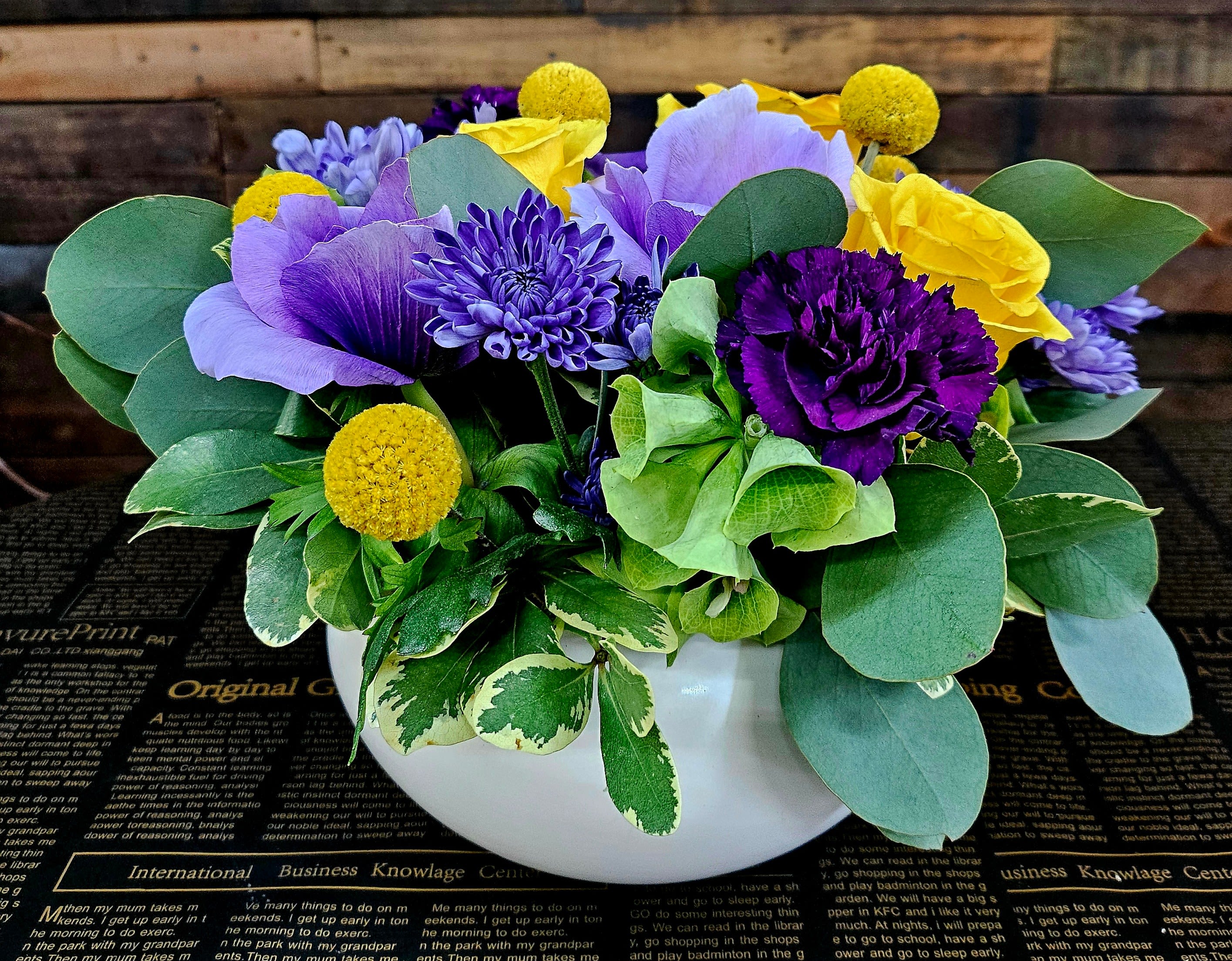 Purple and yellow floral arrangement in a white bowl vase