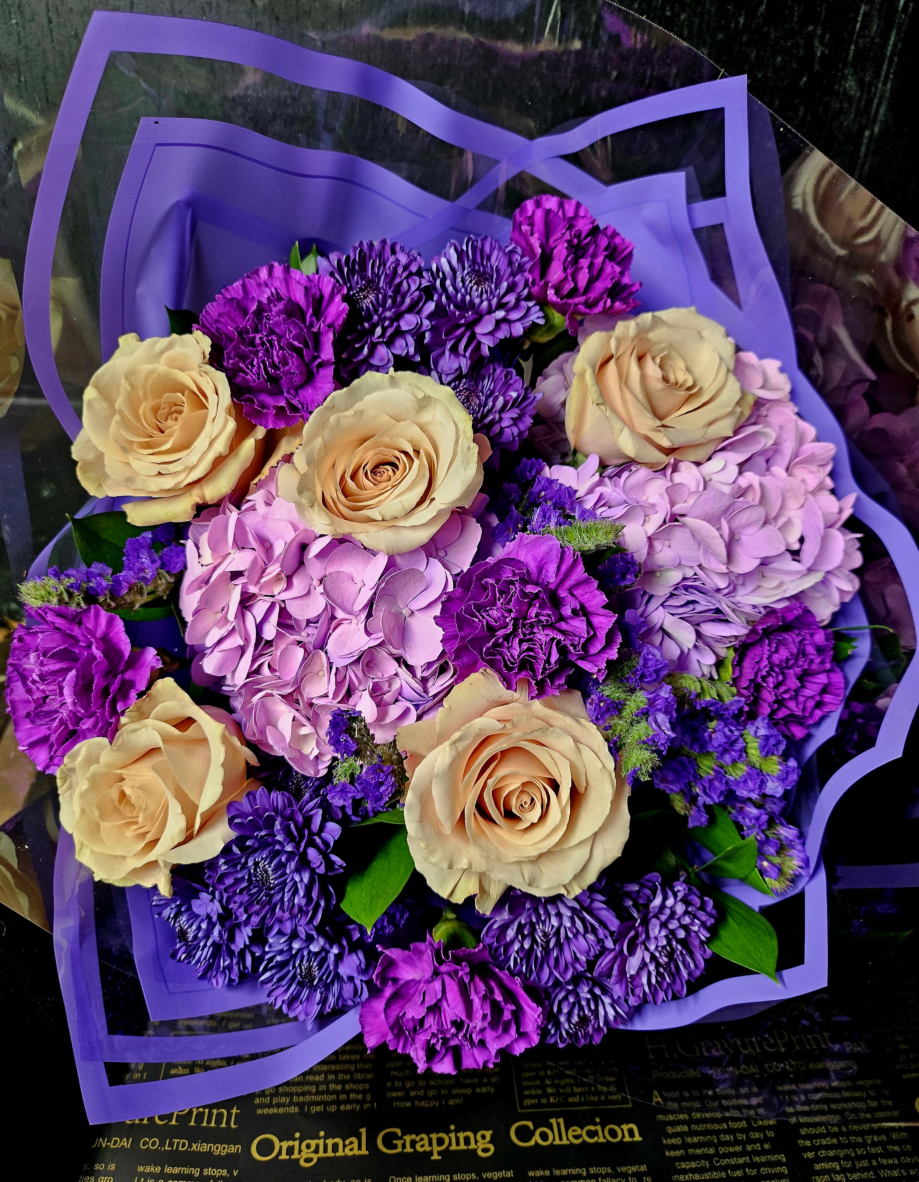 Bouquet of peach roses, purple chrysanthemums, and pink hydrangeas wrapped in purple paper