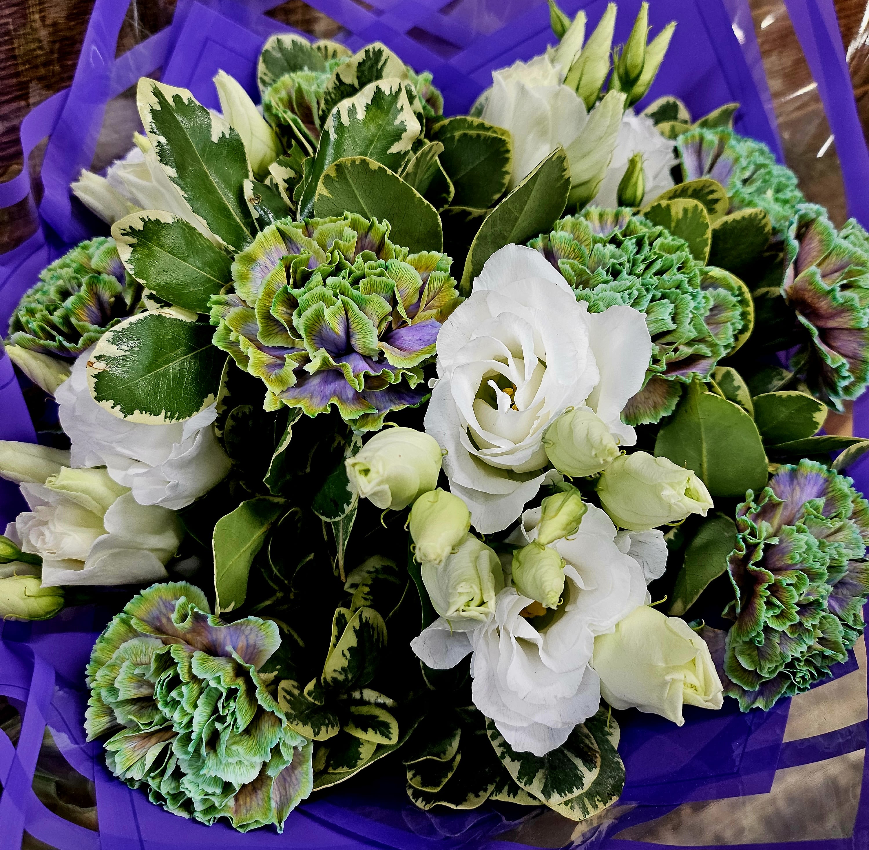 Bouquet of white lisianthus and green-purple carnations wrapped in purple paper