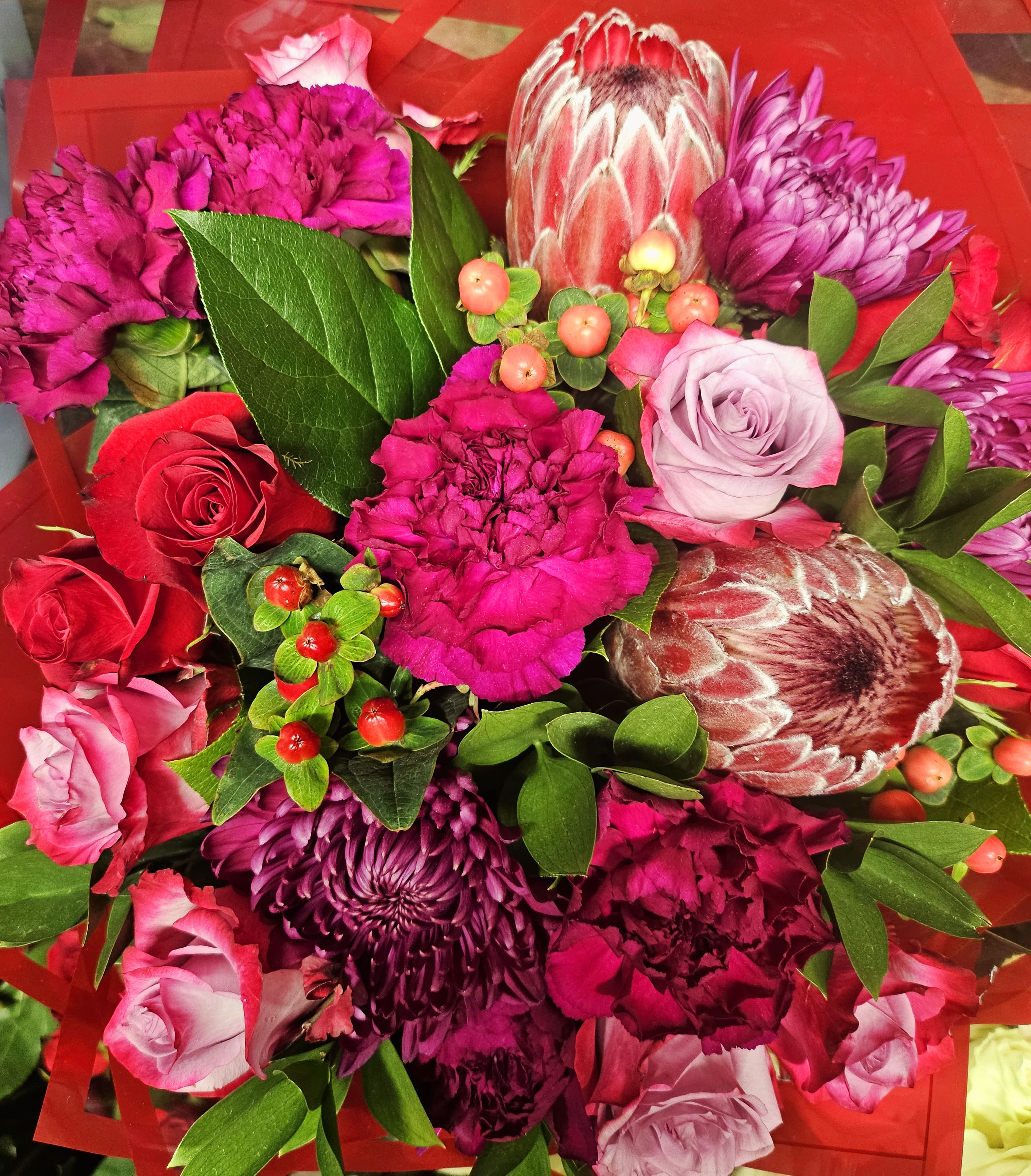 Bouquet of pink and purple flowers with red roses and green foliage