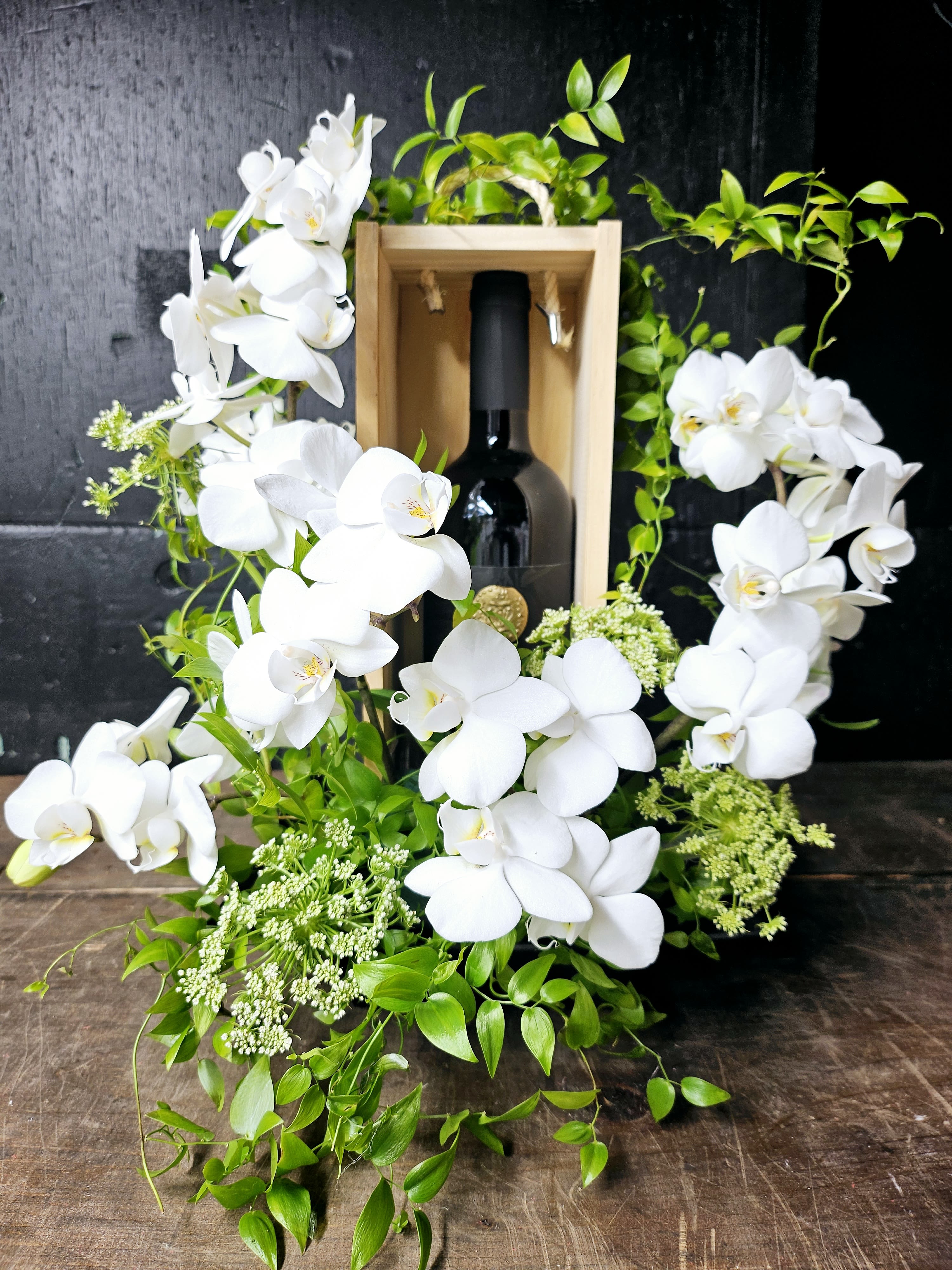 White orchids arranged around a wine bottle in a wooden box