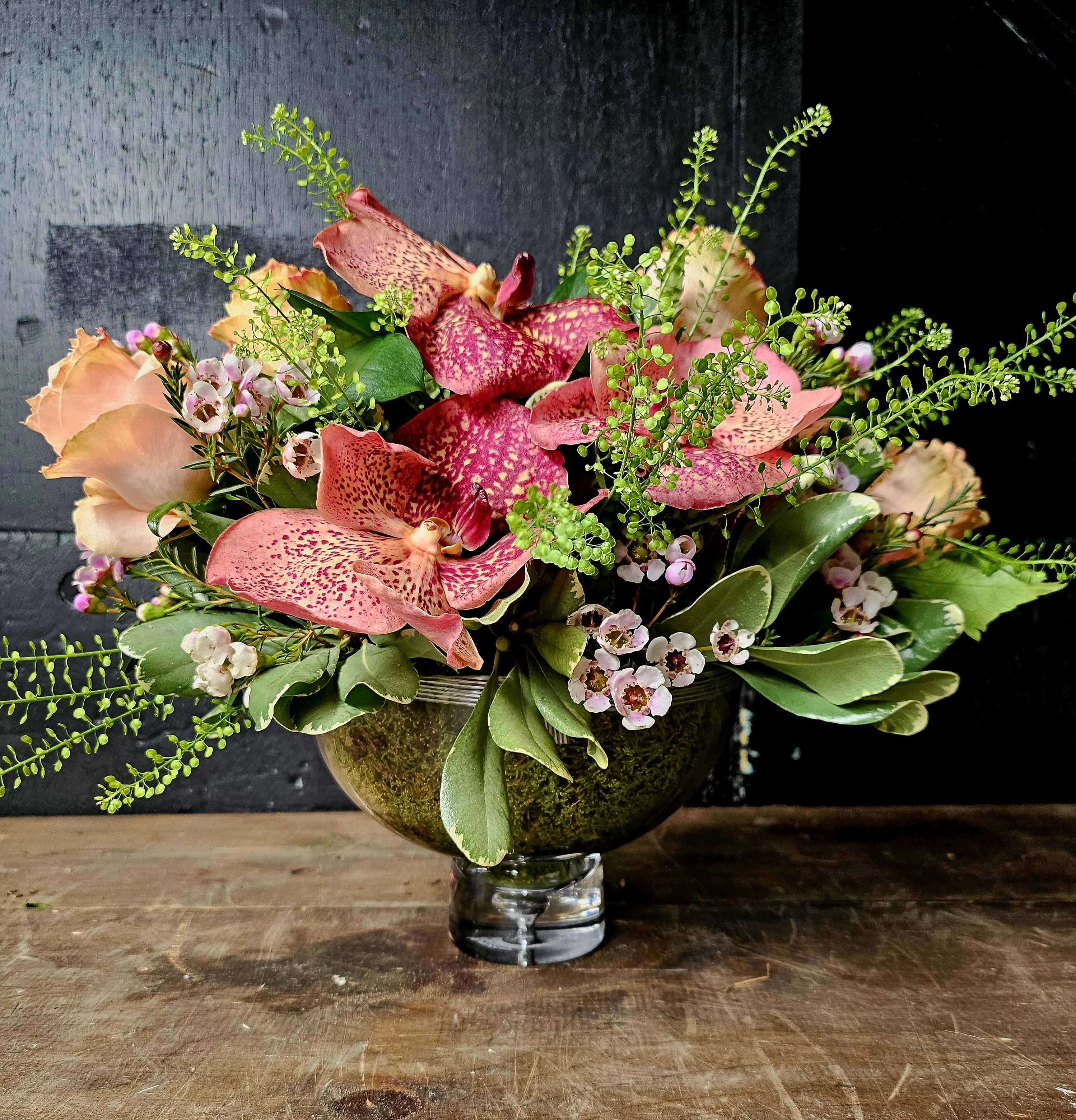 Pink speckled orchids and peach roses in a glass vase