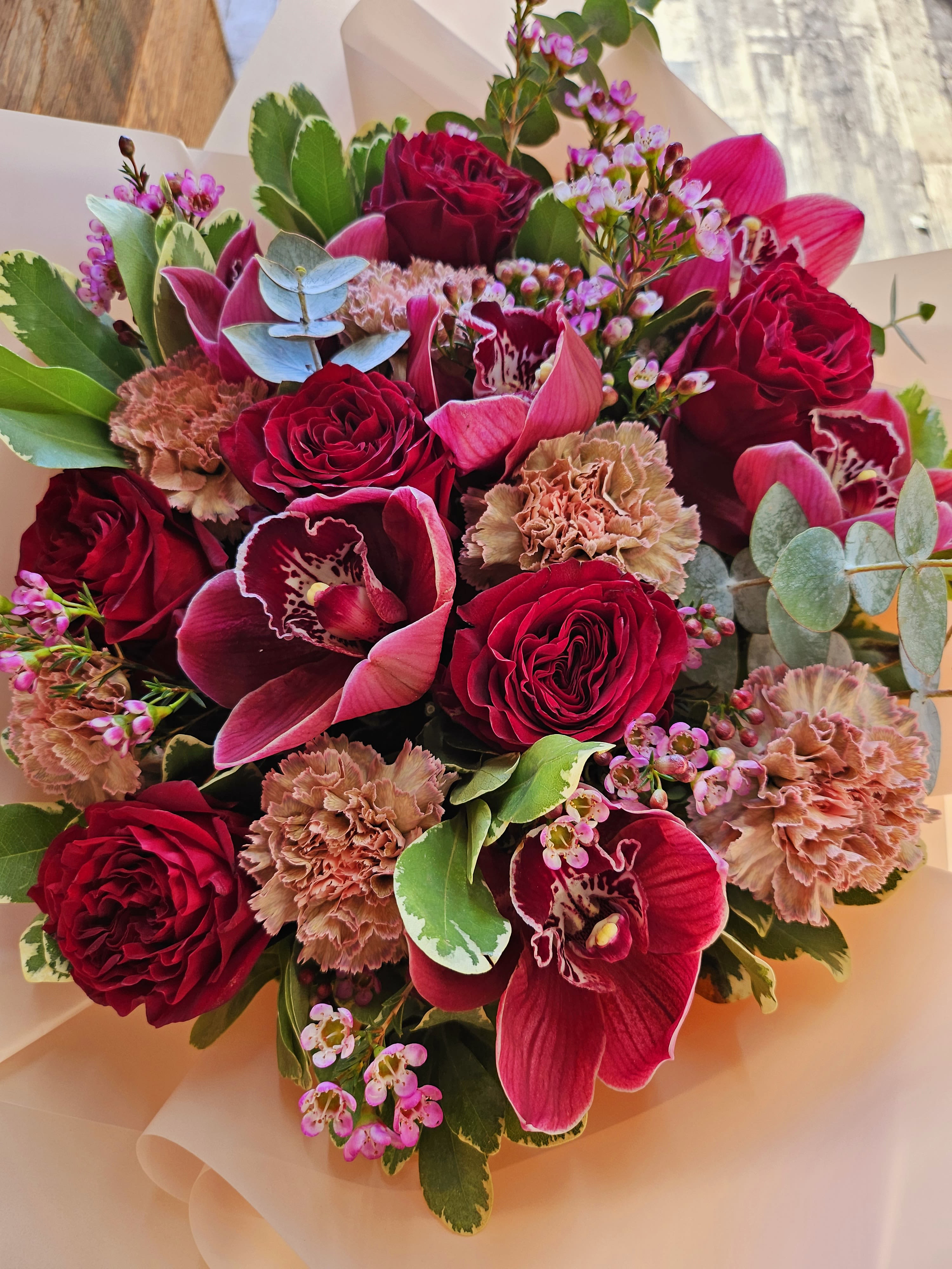 Bouquet of red roses, pink orchids, and carnations in pale wrapping