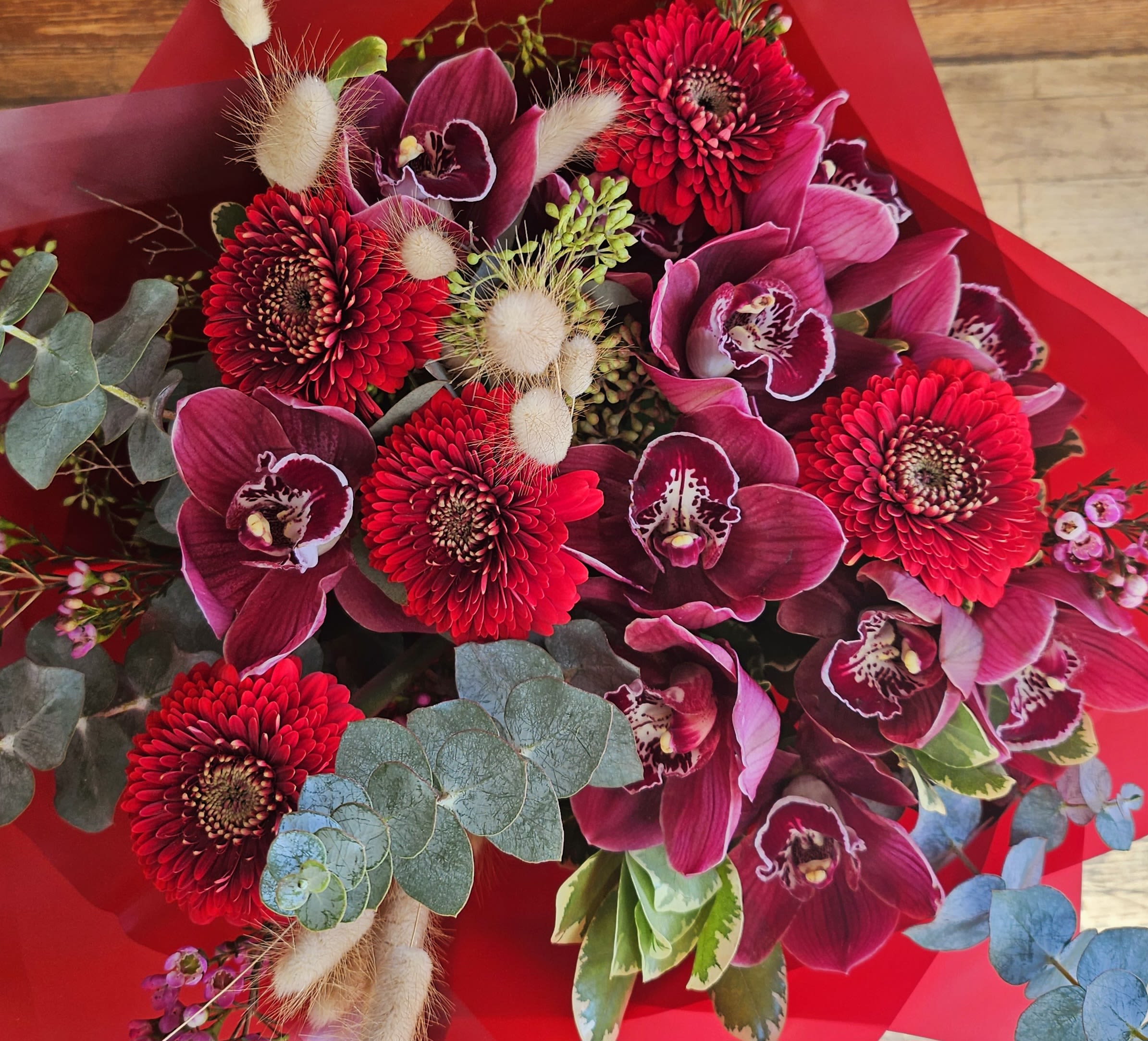 Bouquet of red gerbera daisies and magenta orchids wrapped in red paper
