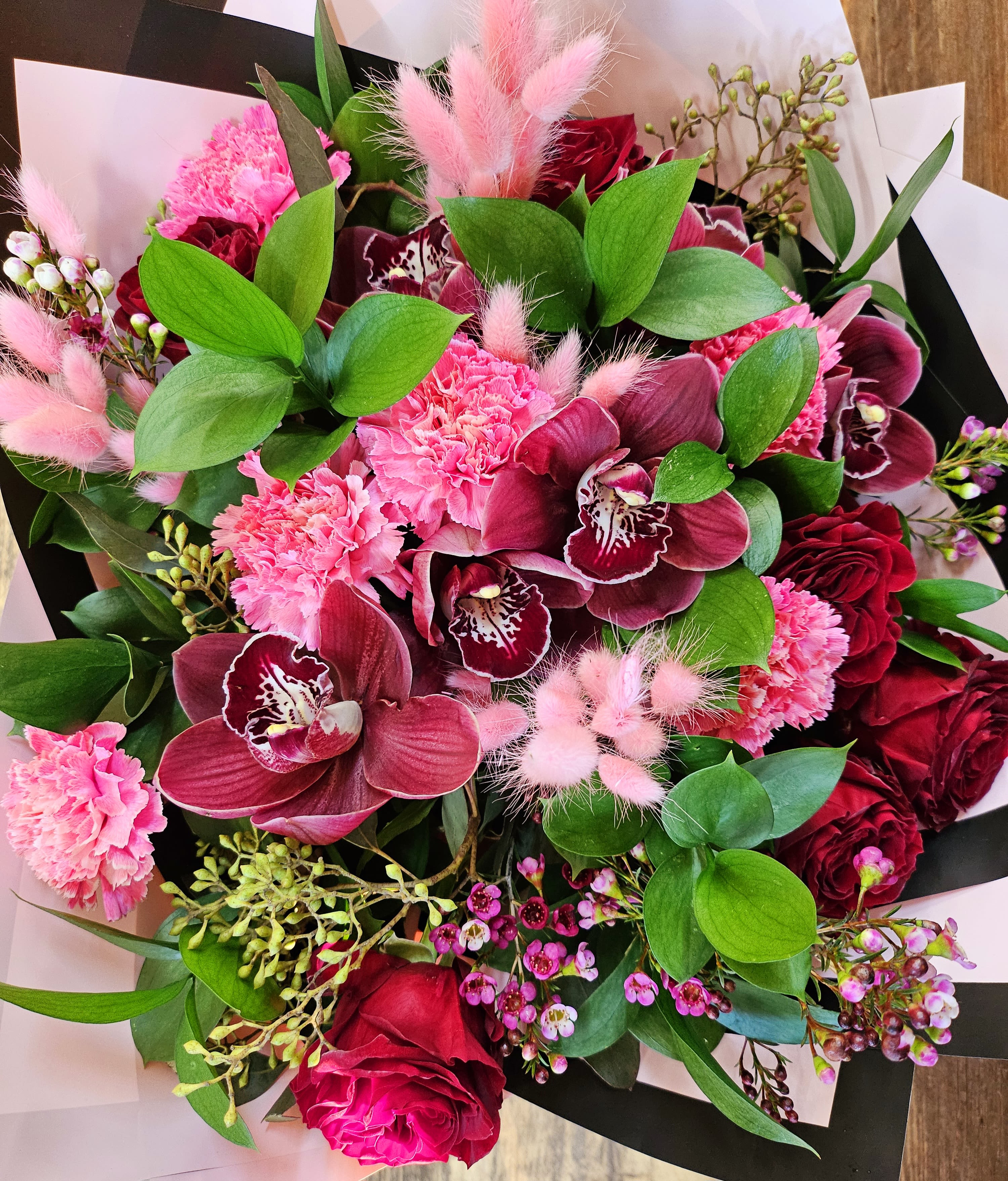 Bouquet of pink and burgundy flowers with green foliage and black-and-white wrap