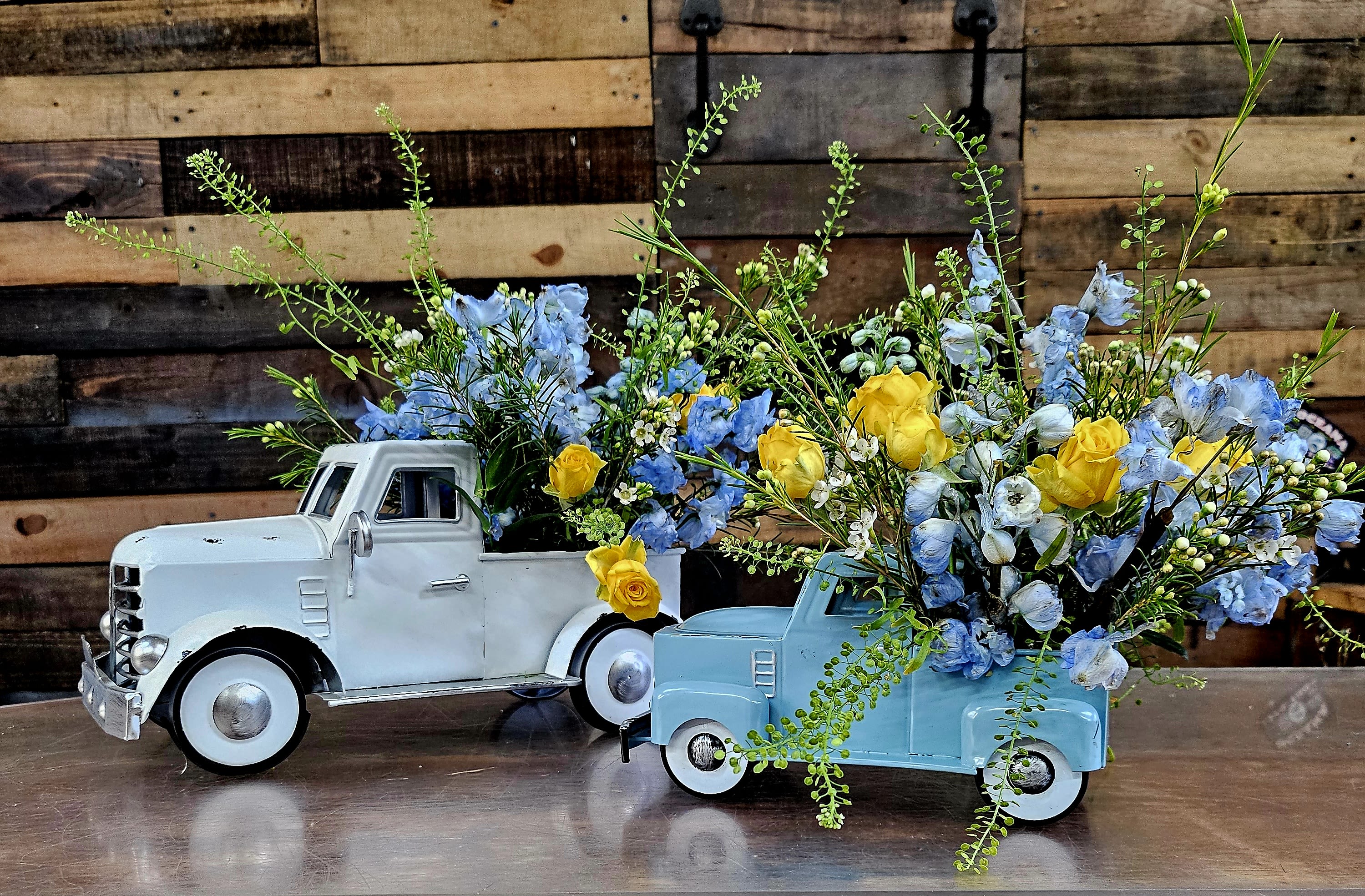 Two toy pickup trucks filled with blue and yellow flowers