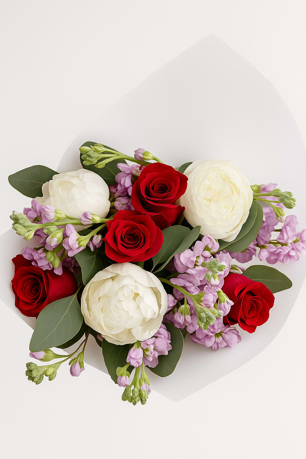 Bouquet of red roses, white ranunculus, and lavender flowers in white paper