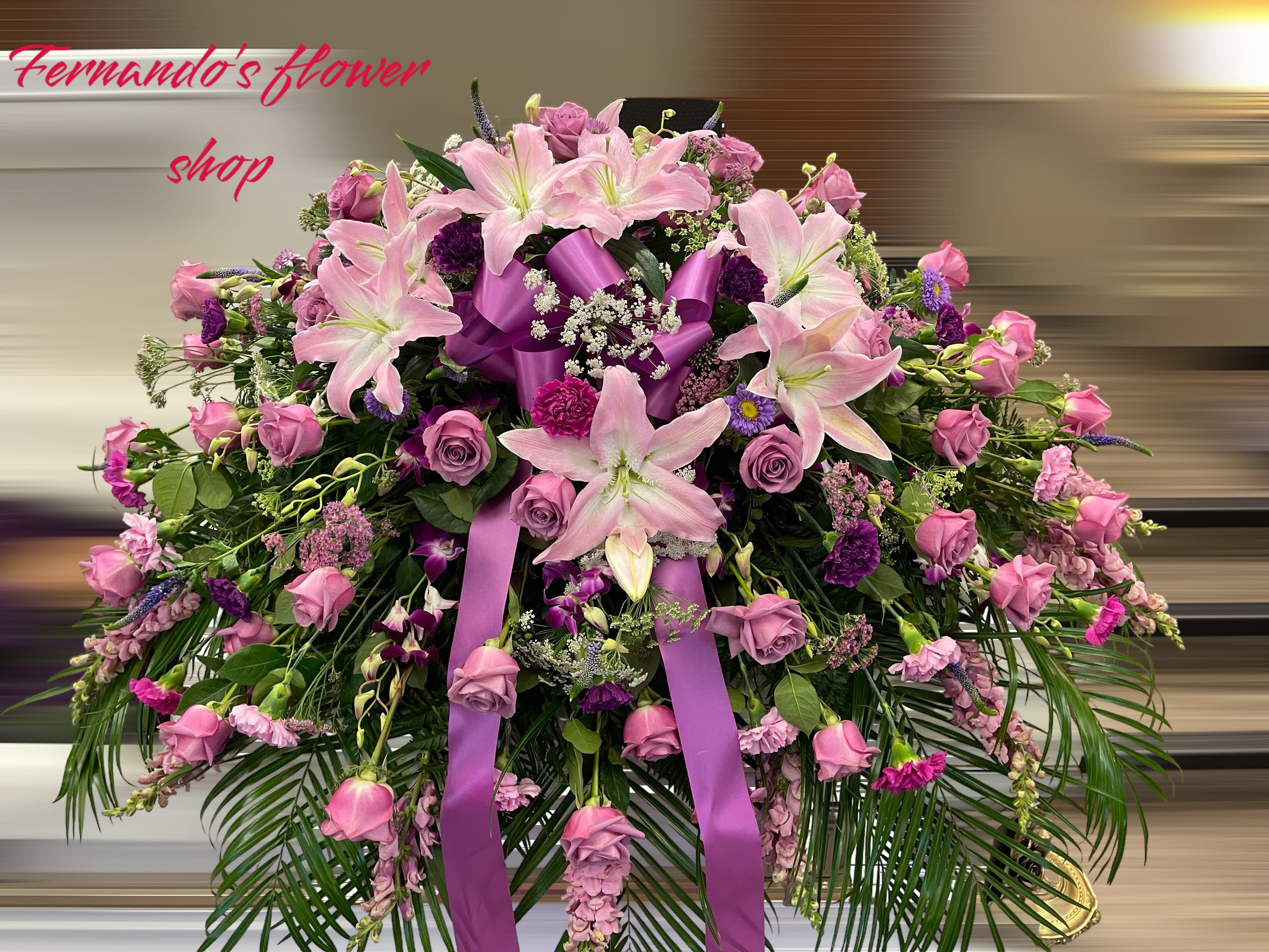 Large pink and purple lily and rose spray with bow and palm fronds on a stand