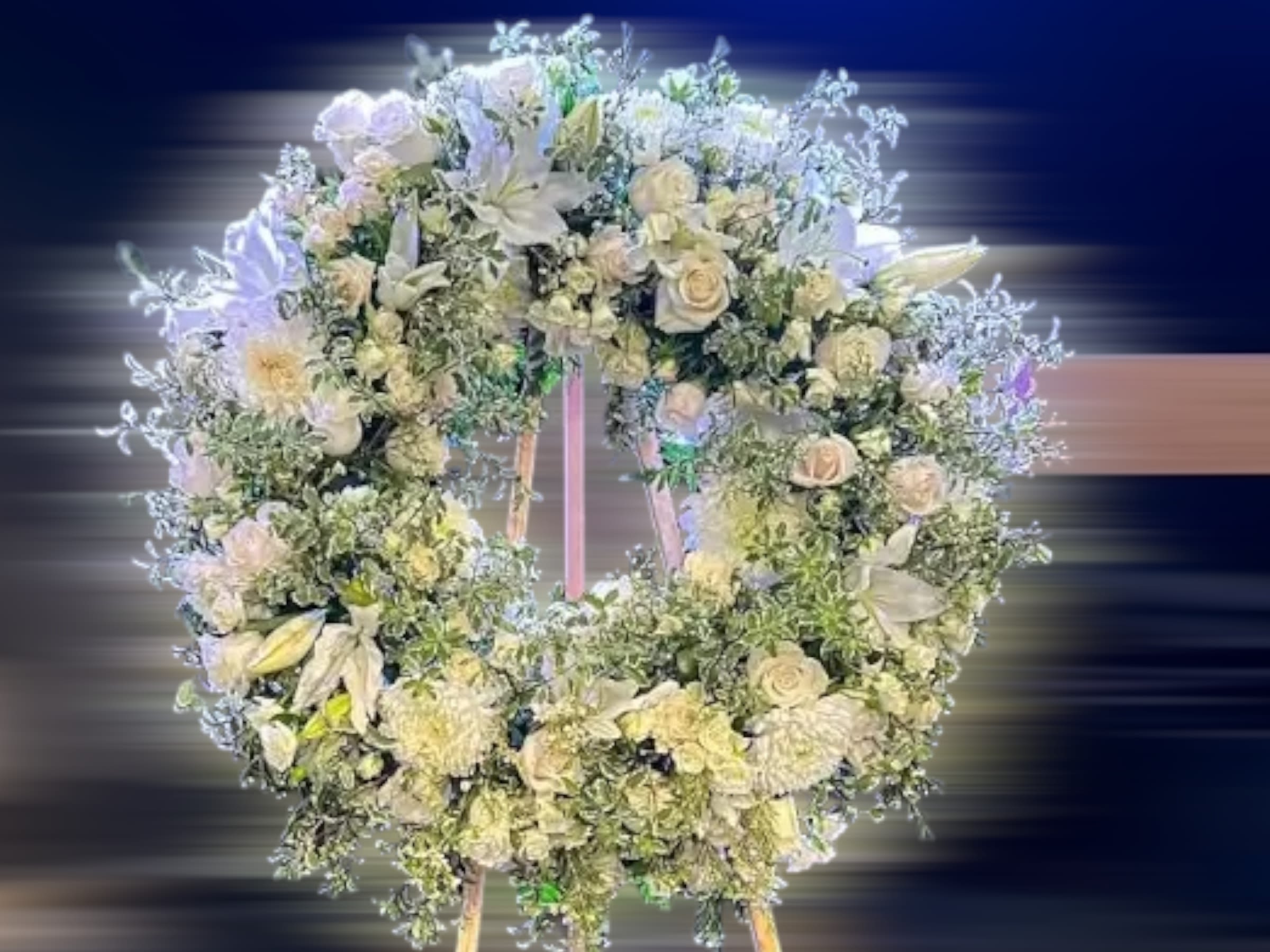 Large white floral wreath with roses and lilies displayed on a wooden easel