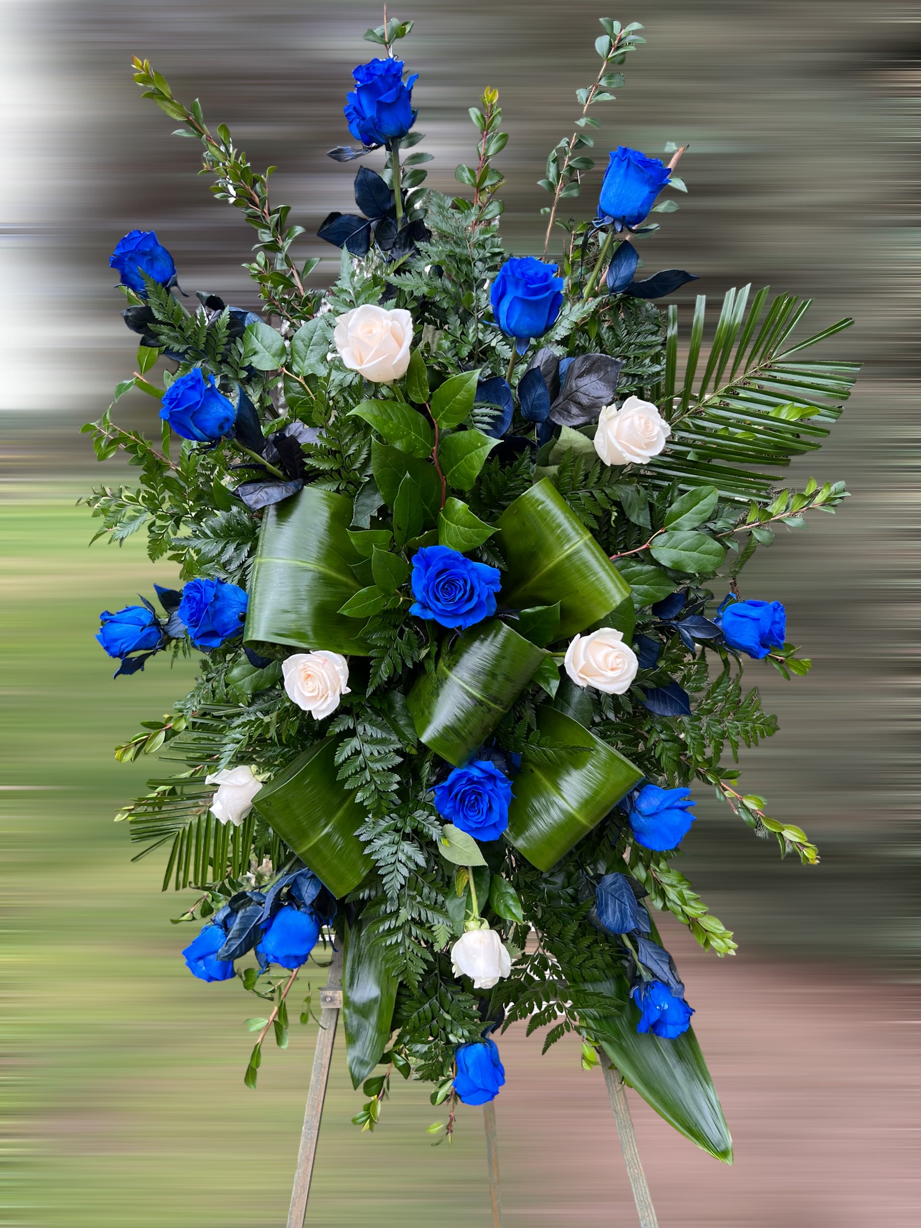 Standing spray of bright blue and white roses with large glossy green leaves on an easel