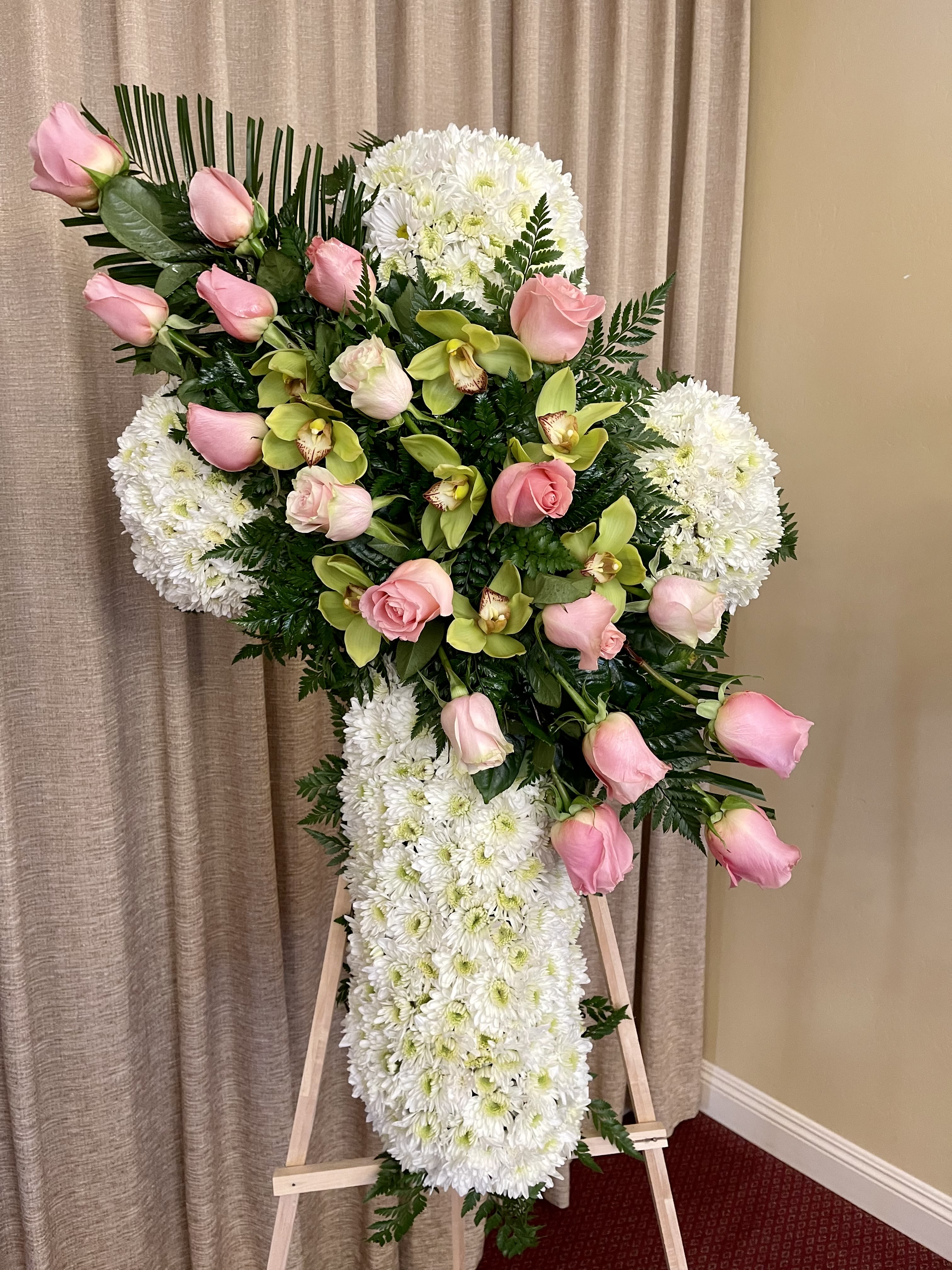 Standing white floral cross with pink roses and green orchids on a wooden easel