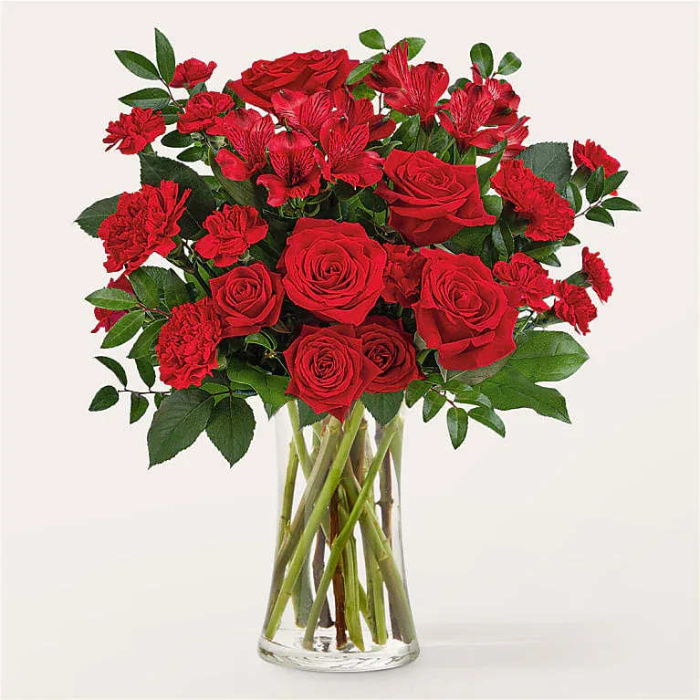 Arrangement of red roses, carnations, and alstroemeria in a clear glass vase