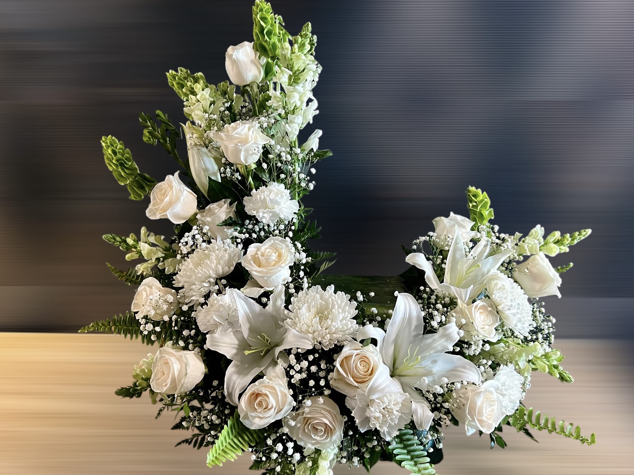 Tall crescent-shaped arrangement of white roses, lilies, and mums with green accents