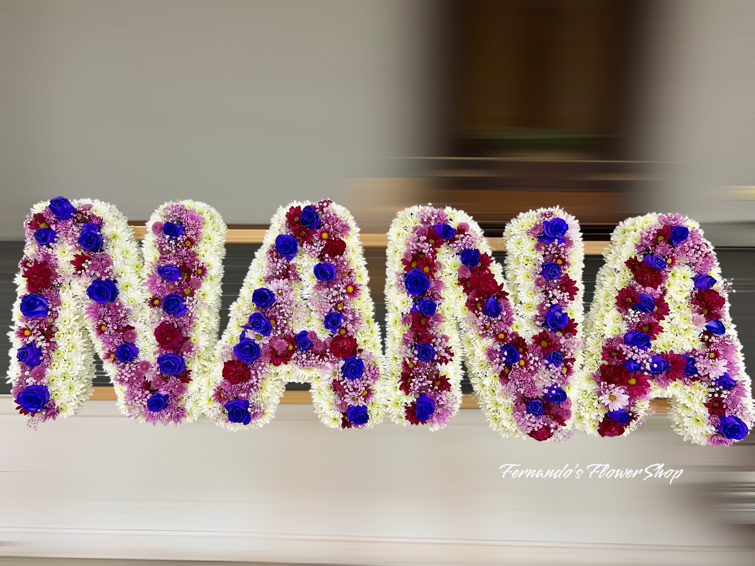 Funeral tribute letters spelling NANA in white flowers with purple and blue accents.