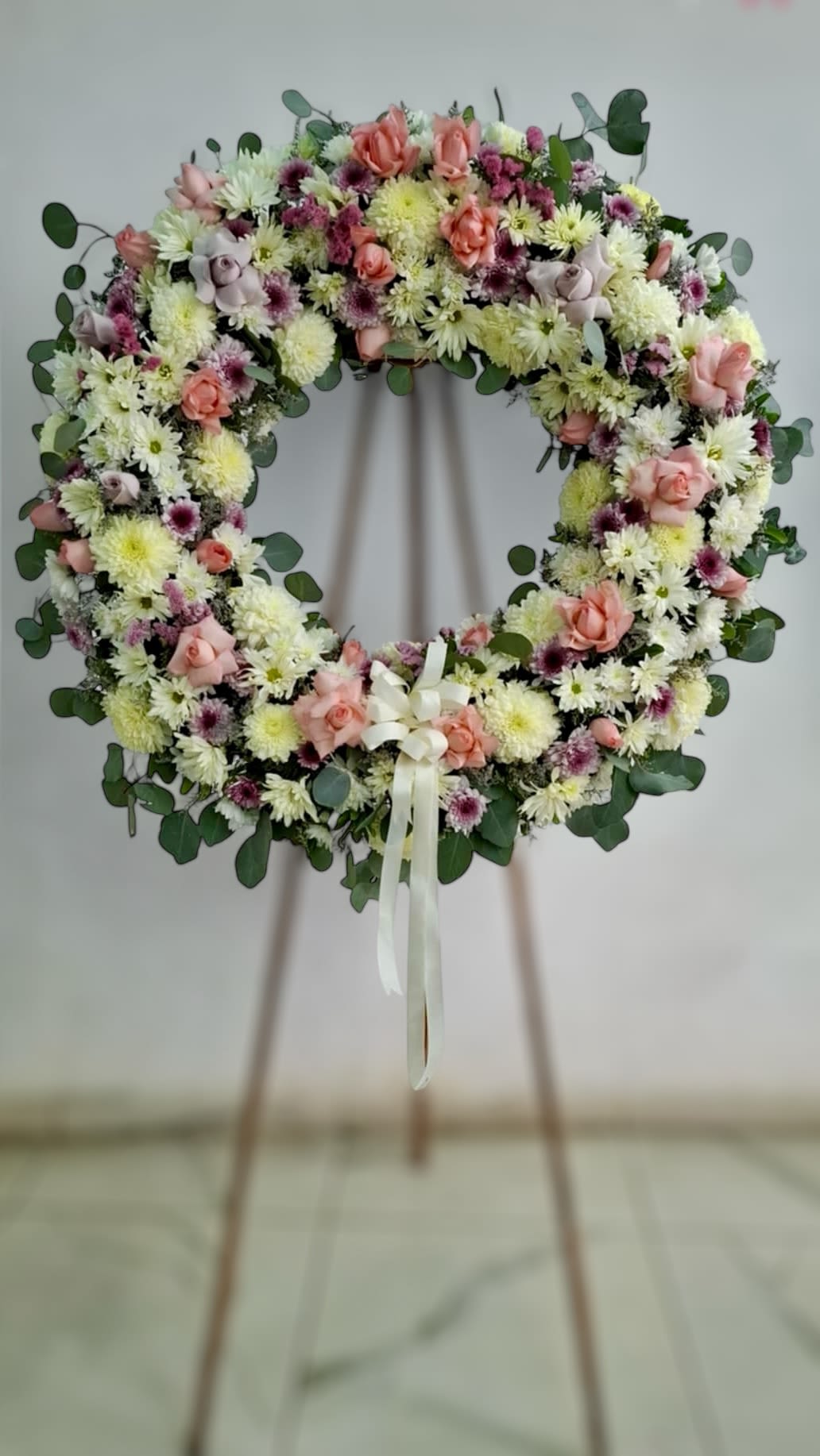 Large floral wreath of white mums and pink roses on a wooden easel with ivory ribbon.