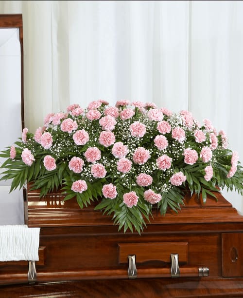 Pink carnation casket spray with white filler flowers on a wooden casket