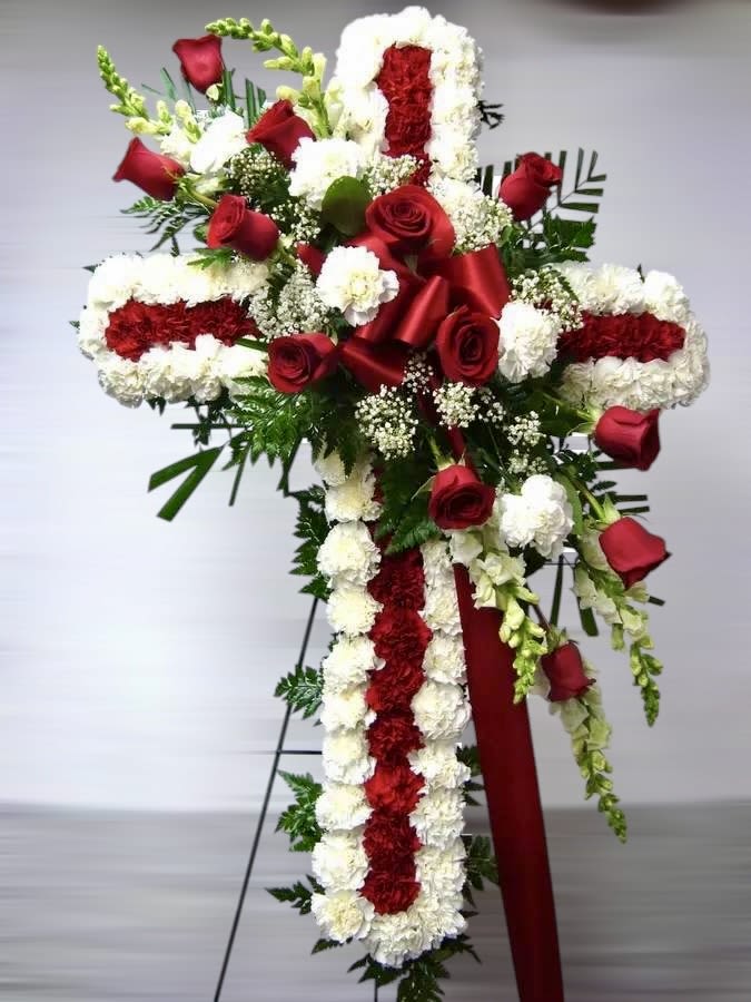 Tall red and white floral cross on an easel with red roses, carnations, and a satin ribbon