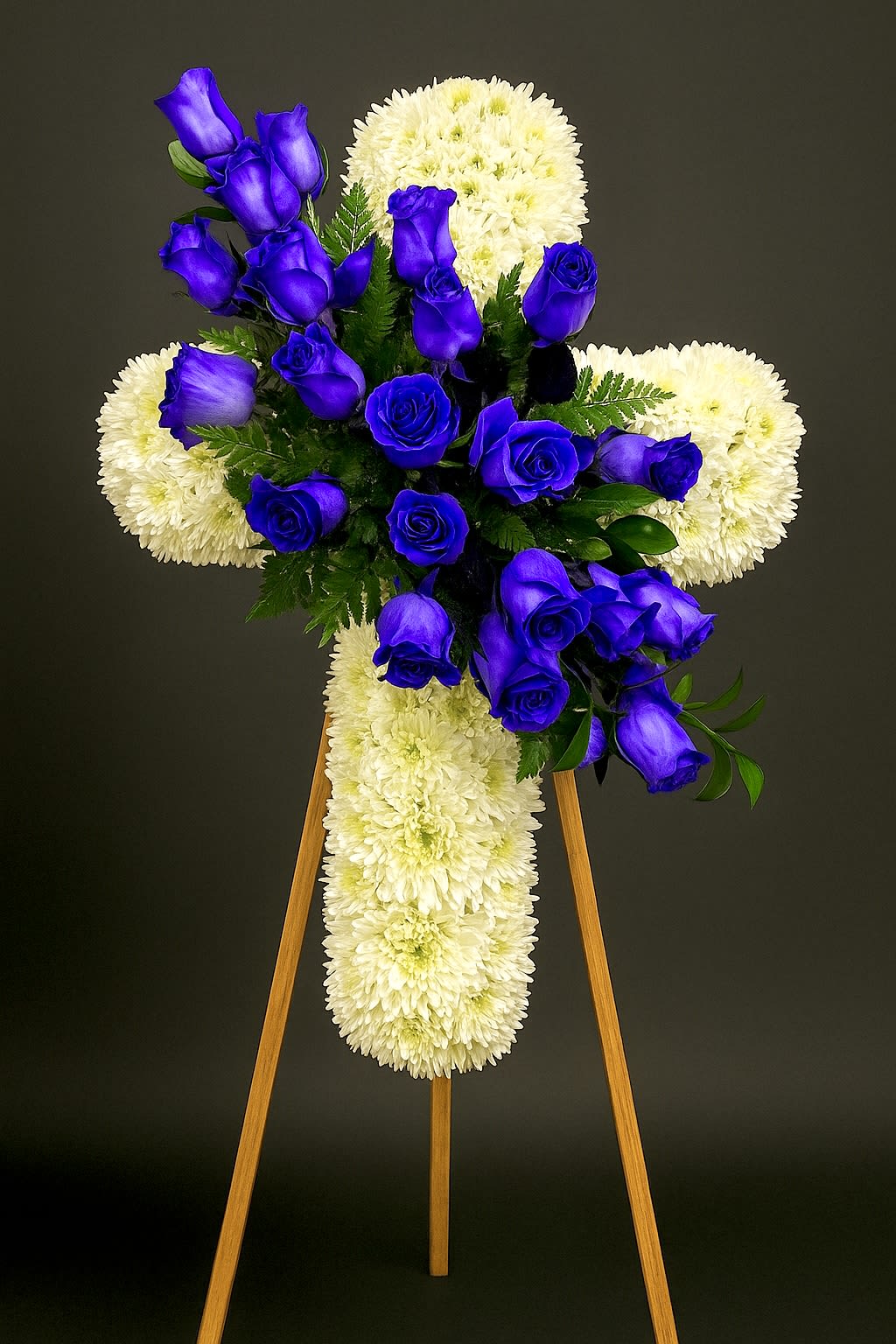 Standing white chrysanthemum cross with cluster of vivid blue roses on a wooden easel