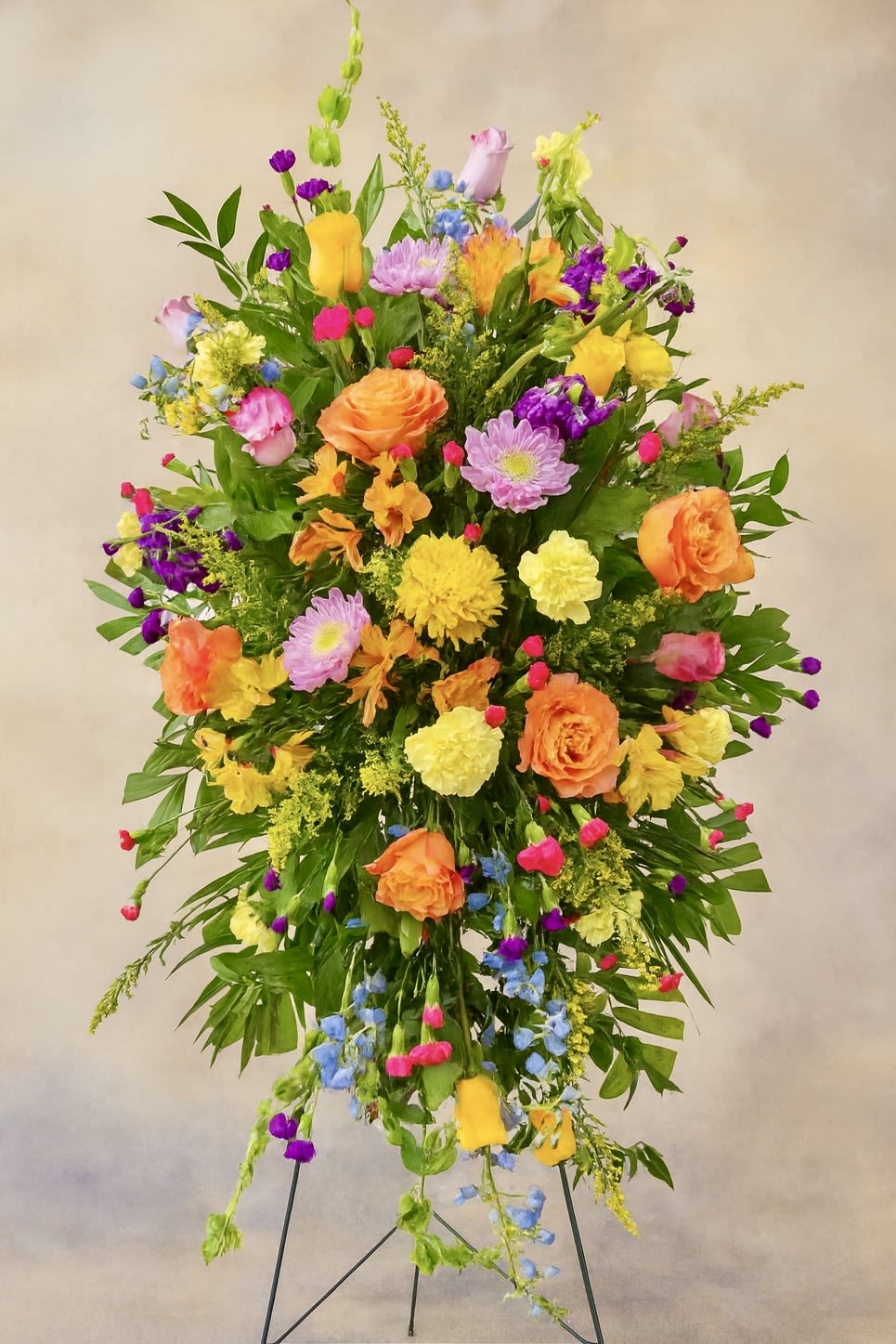 Tall multicolor standing spray with orange roses and yellow blooms on a metal easel