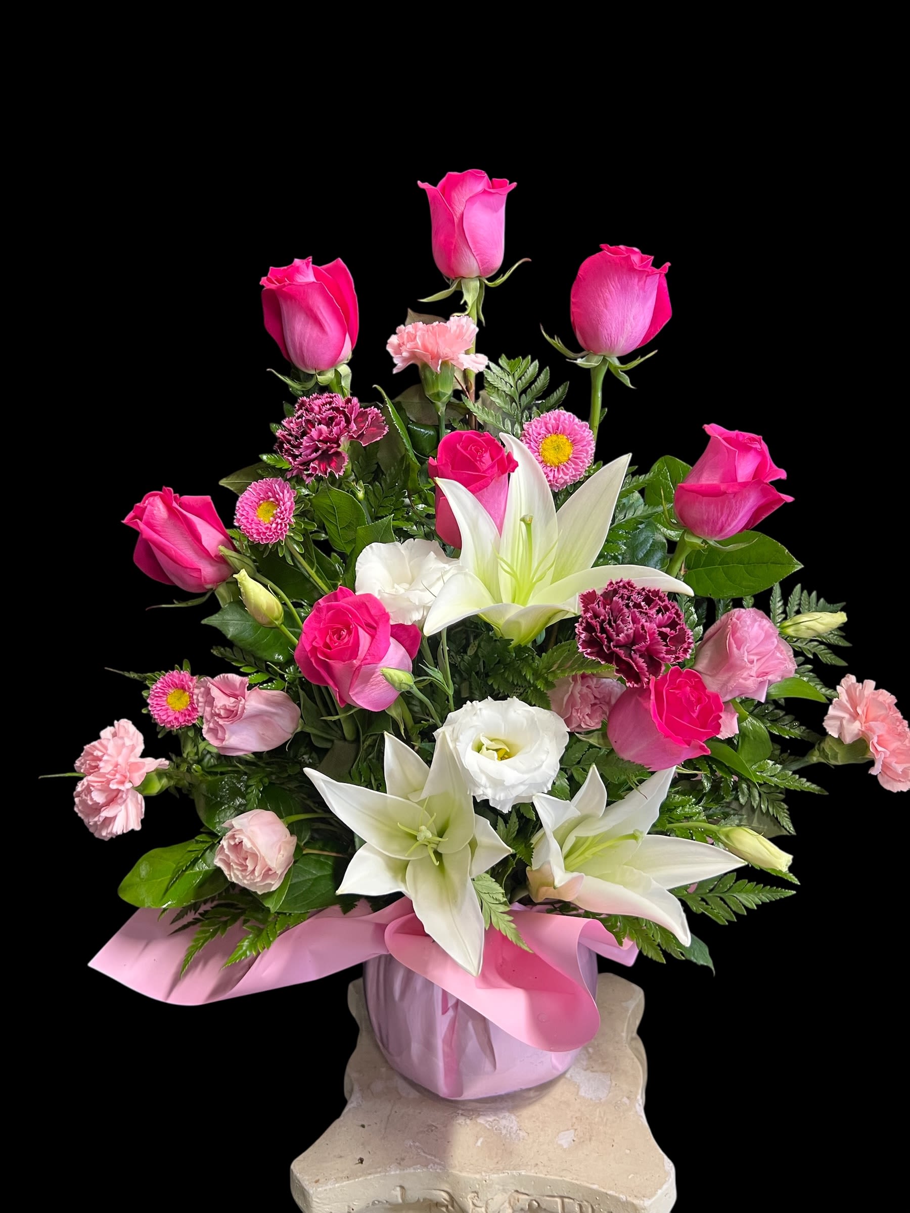 Pink and white arrangement with roses, lilies, and carnations in a pink vase with ribbon