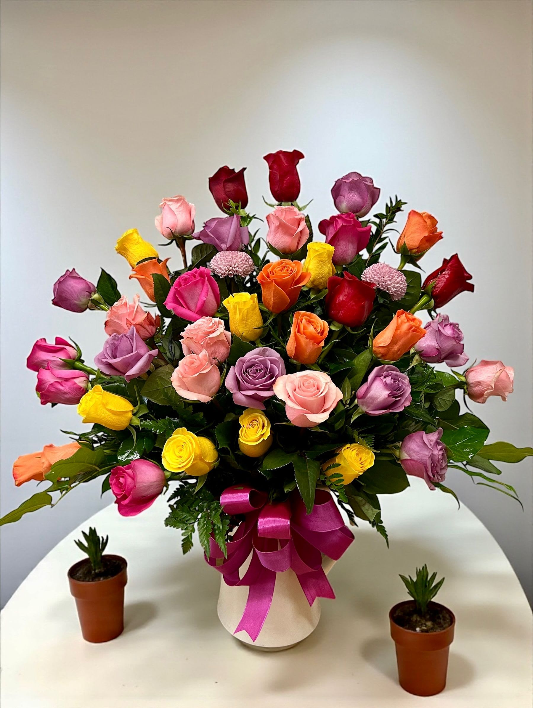 Colorful bouquet of roses in a white vase with a pink ribbon