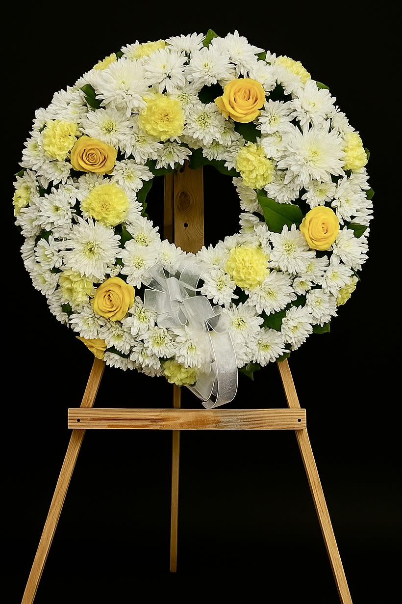 White and yellow floral wreath on a wooden easel with a ribbon bow
