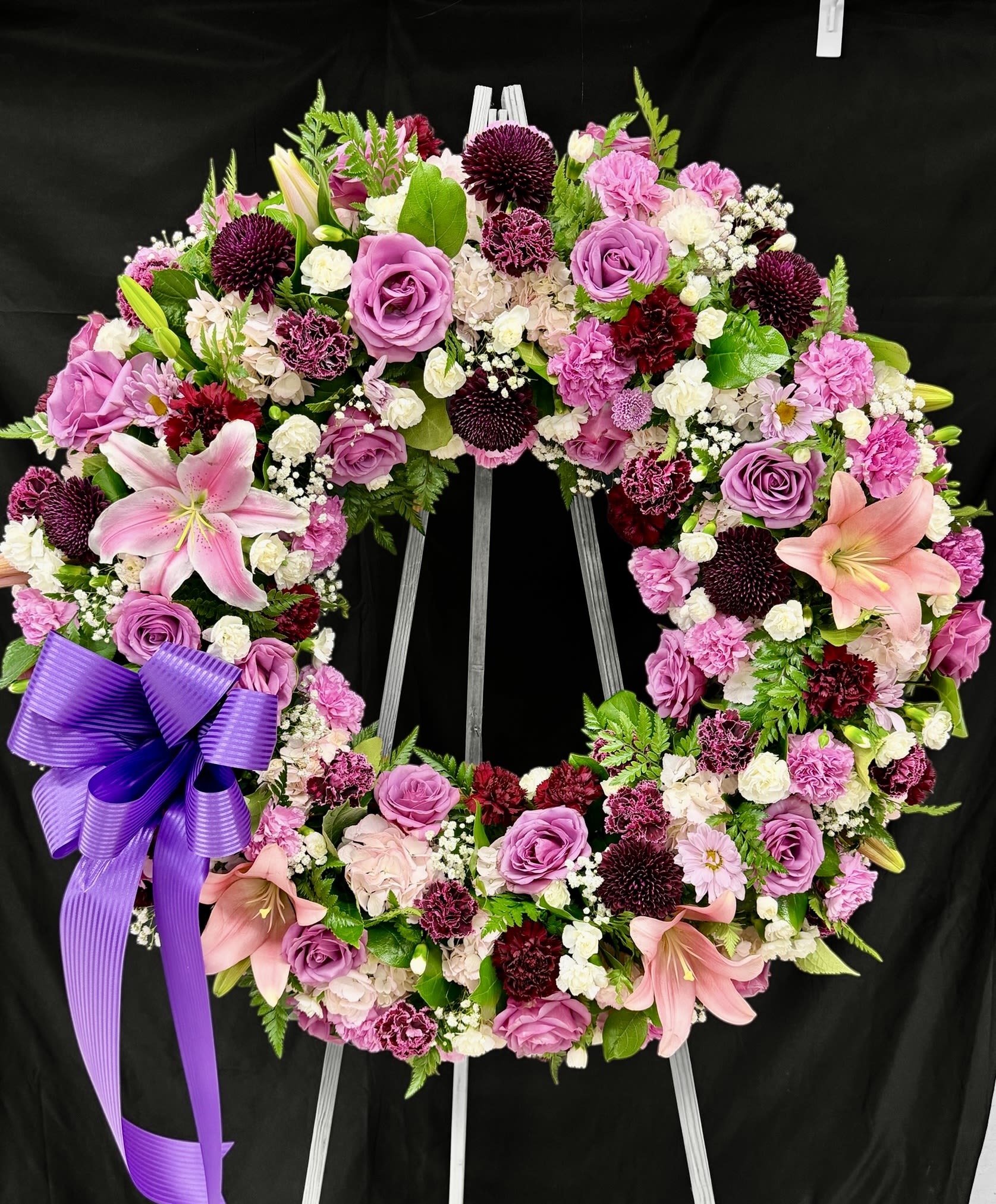 Circular floral wreath with pink and purple flowers and a purple ribbon bow