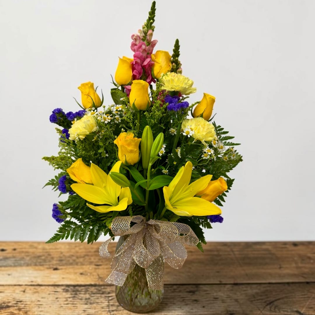Yellow roses and lilies with pink snapdragons in a glass vase