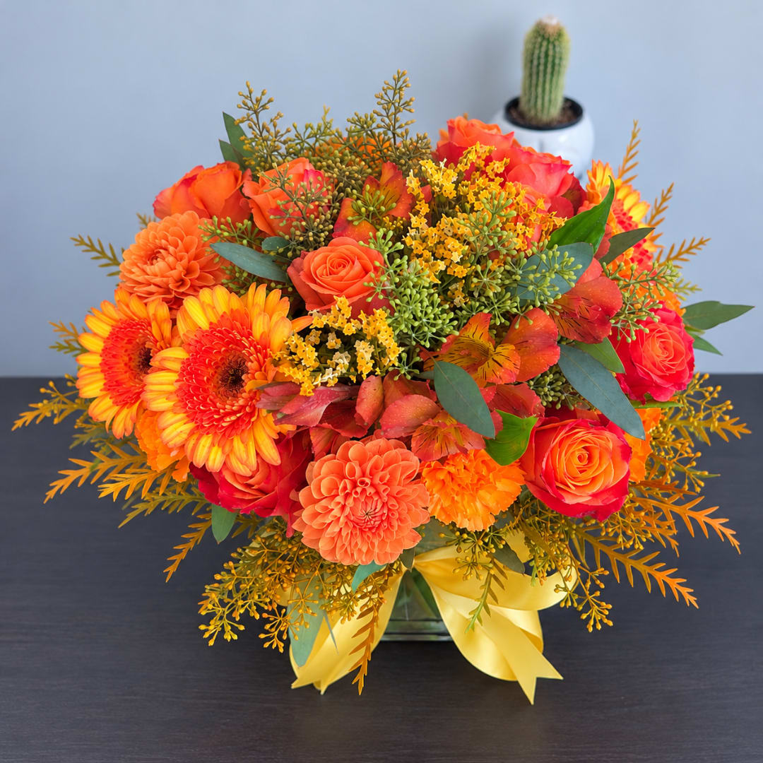 Orange and pink mixed bouquet in a glass vase with a yellow ribbon