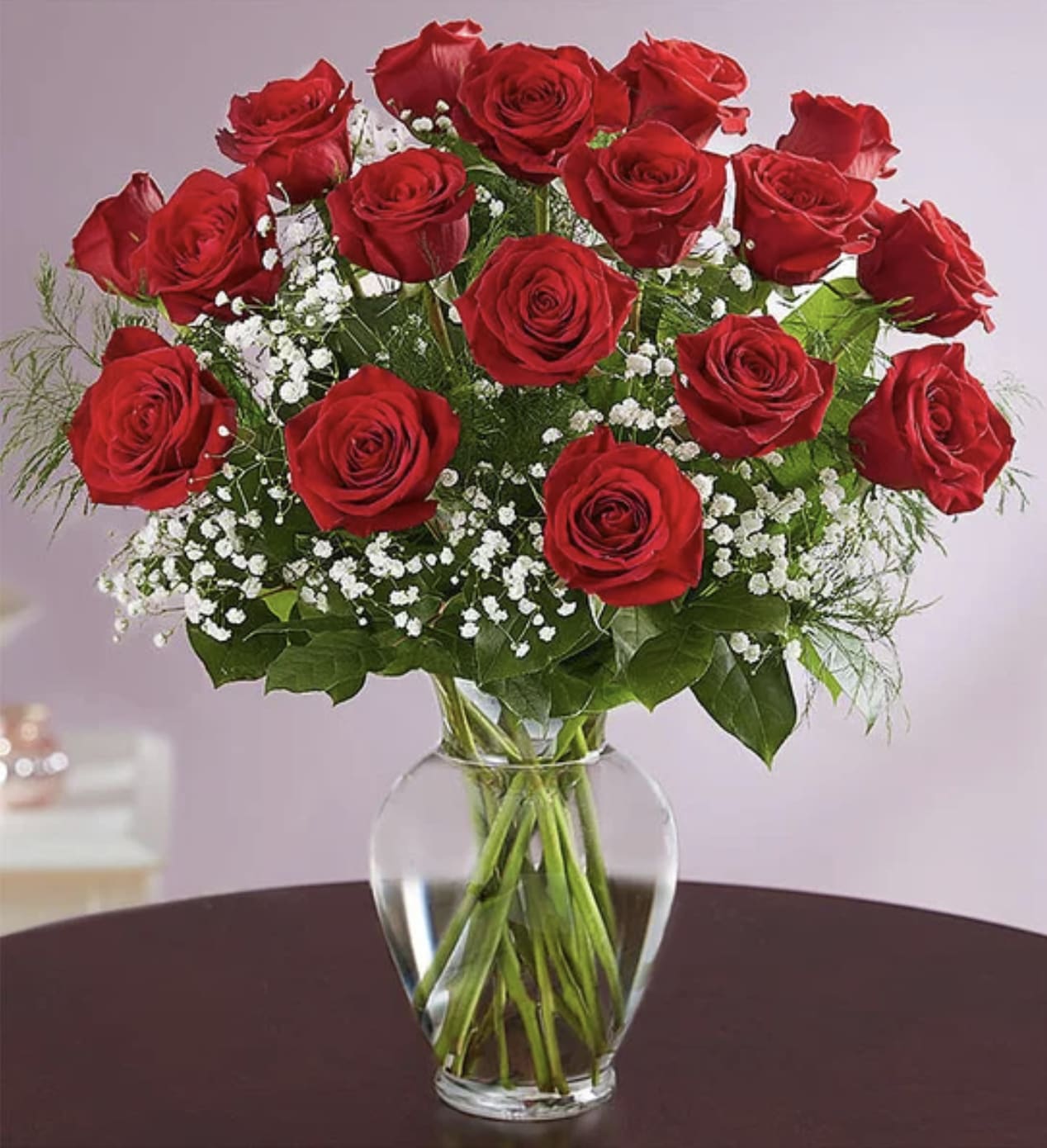 Dozen red roses with white filler flowers arranged in a clear glass vase