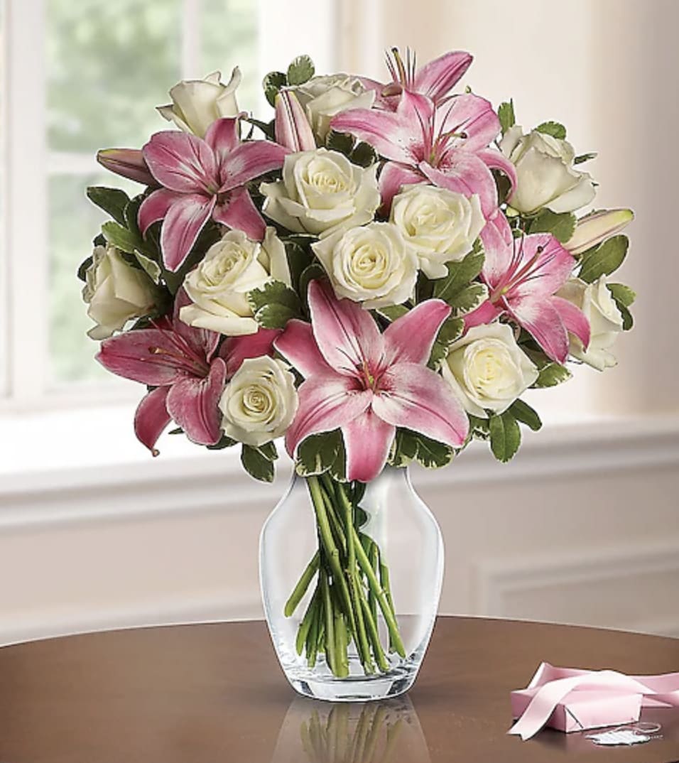 Pink lilies and white roses arranged in a clear glass vase on a table.