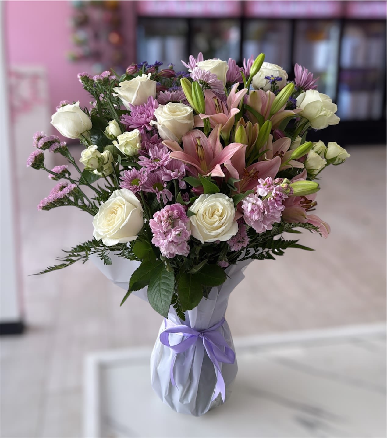 Bouquet of white roses, pink lilies, and purple flowers in wrapped paper