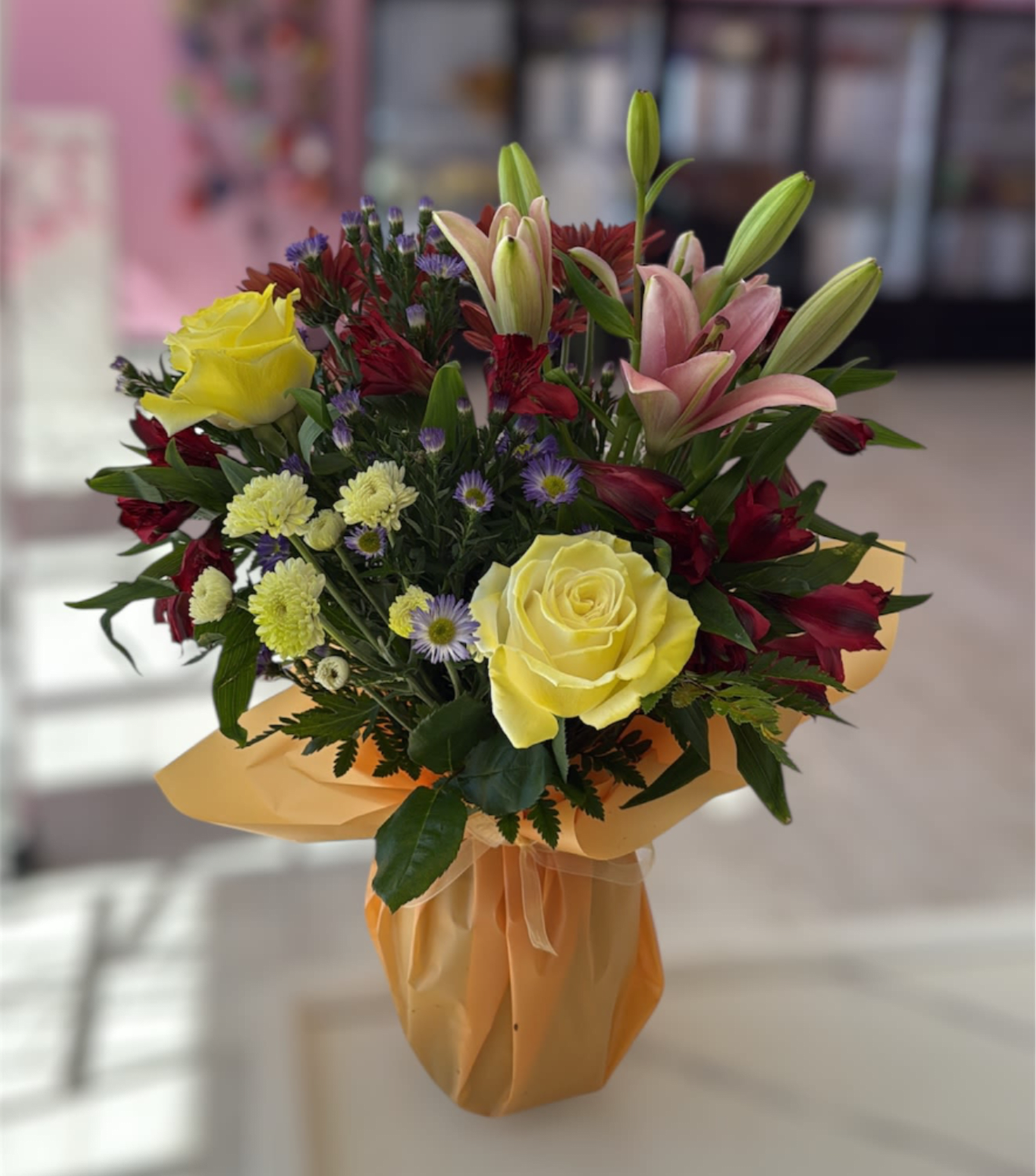 Bouquet of yellow roses, pink lilies, and red flowers wrapped in peach paper