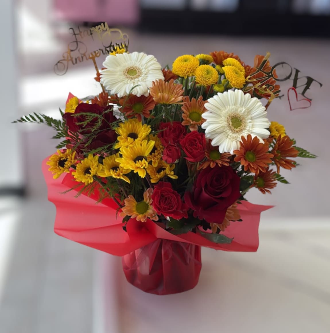 Bouquet of red roses, white gerbera daisies, and yellow mums in pink wrap