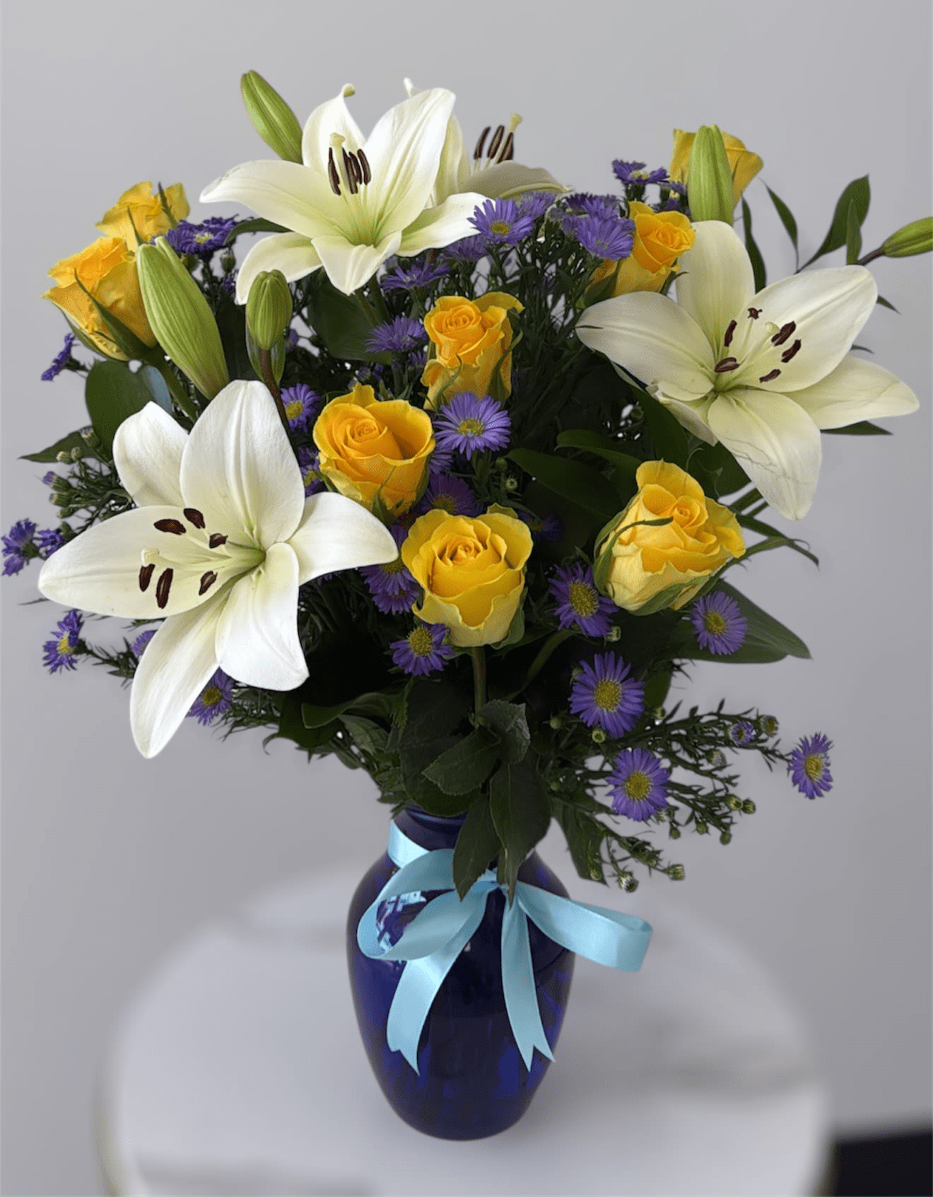 White lilies and yellow roses in a blue vase with a ribbon