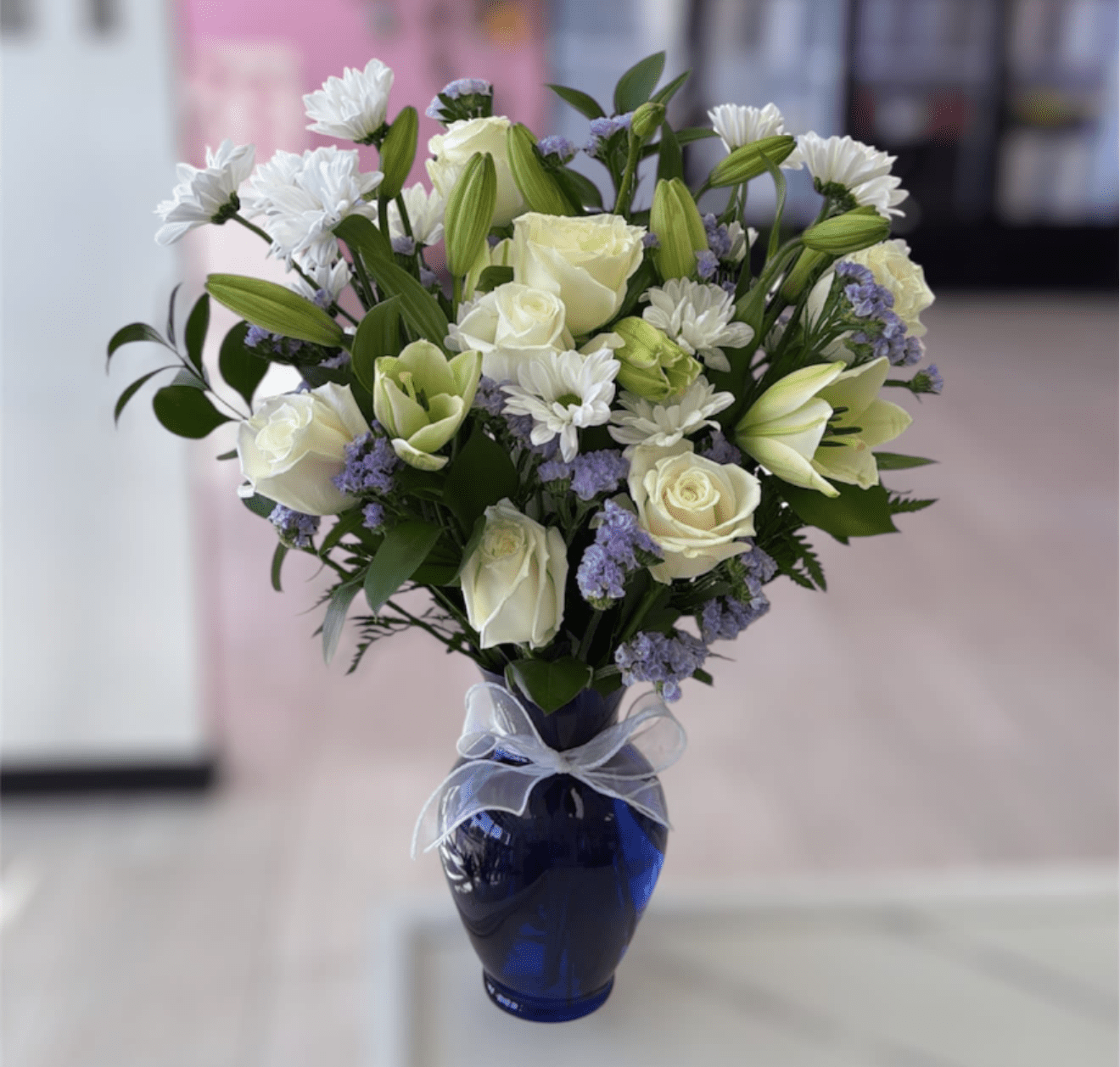 White roses and lilies arranged in a blue vase with a ribbon