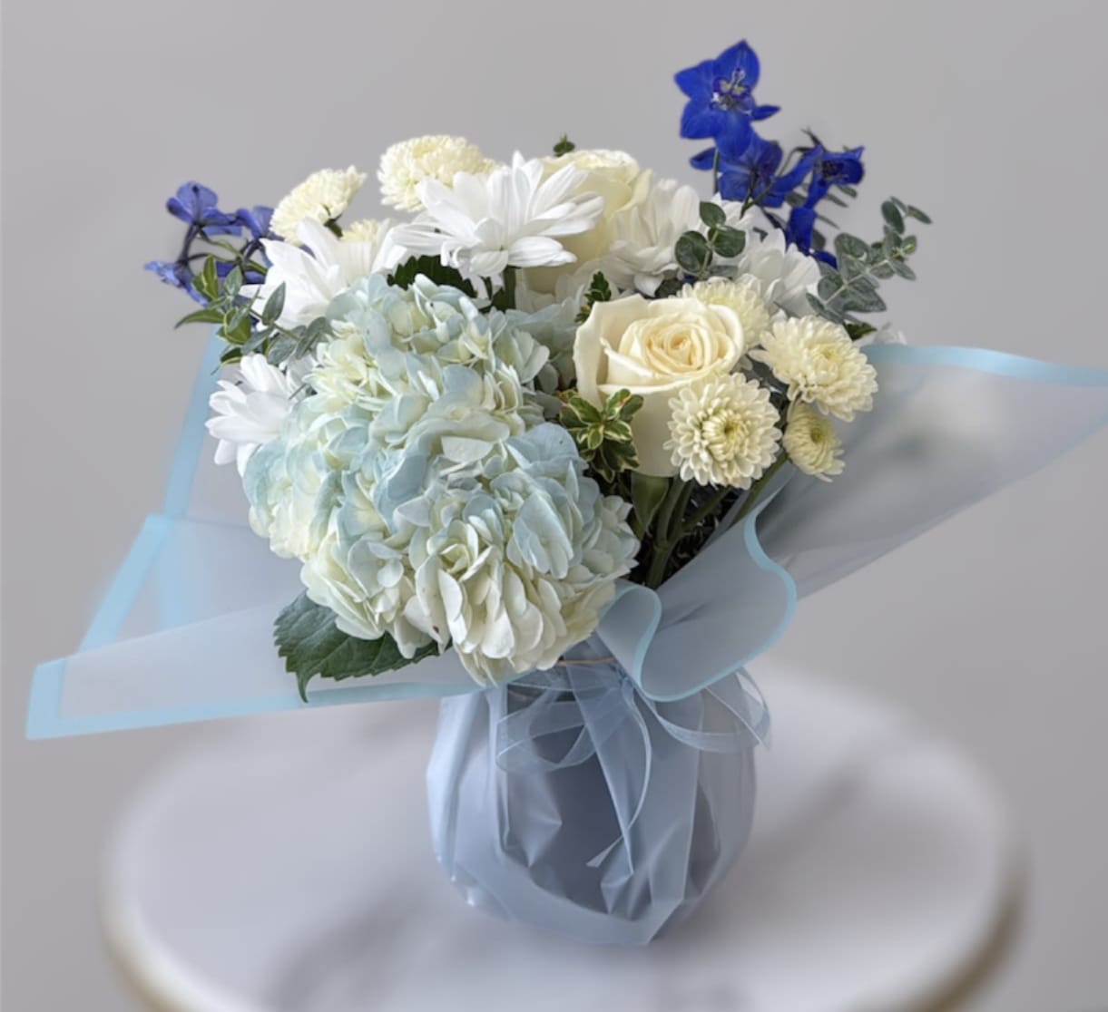 Bouquet of white and pale blue flowers in a wrapped vase
