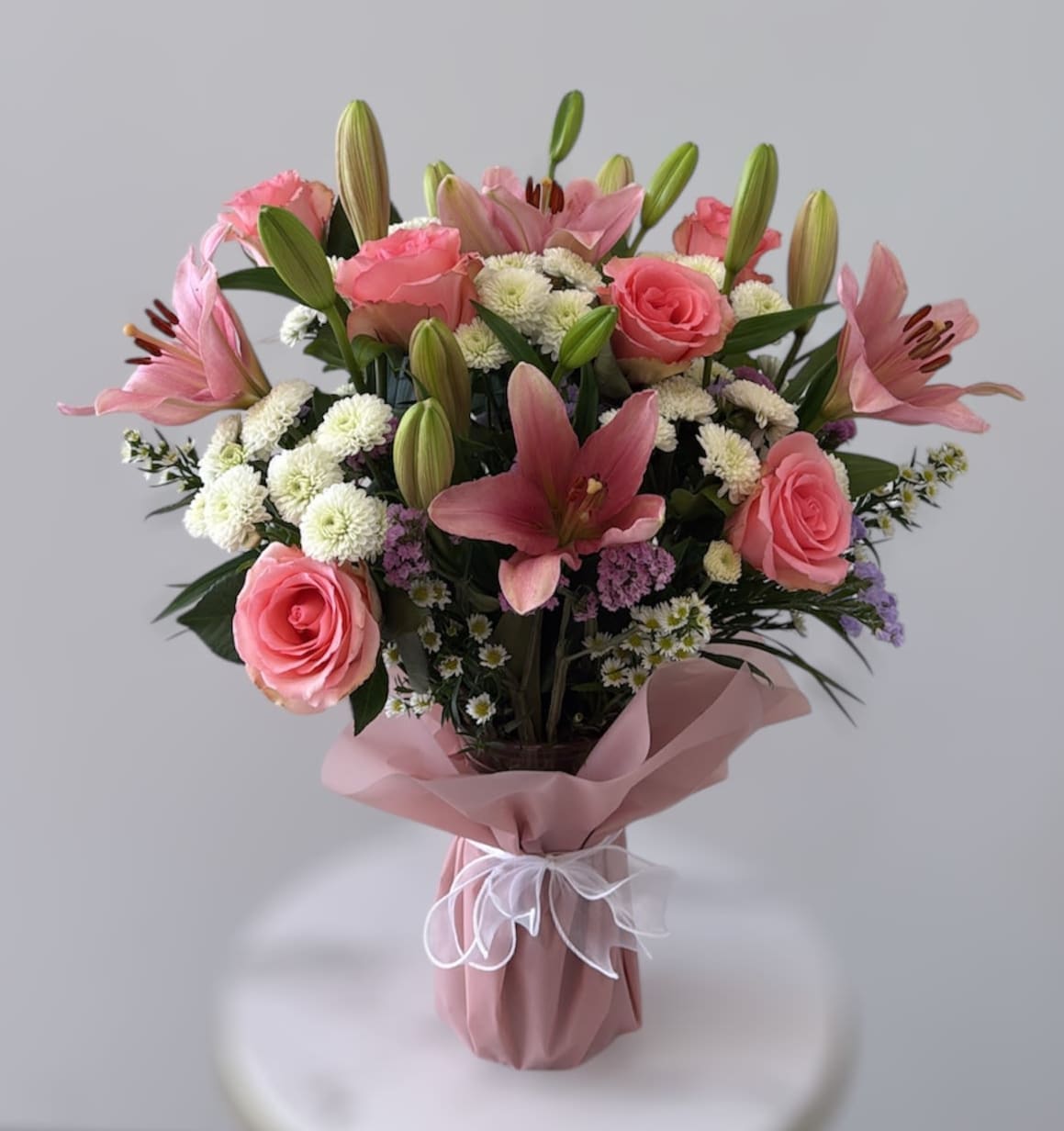 Romance &amp; Roses - Pink roses, lilies and daisies tied with a bow combines everyone's favorite valentine gifts! Because of seasonality and product availability, your arrangement may vary from what is shown, but will be filled to value with the freshest and highest quality, long-lasting flowers available. 