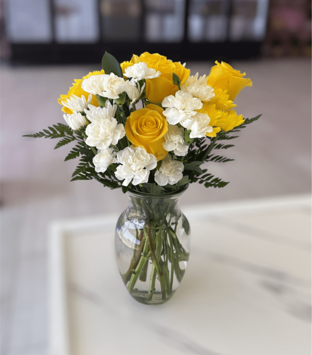 Yellow roses and white carnations in a clear glass vase