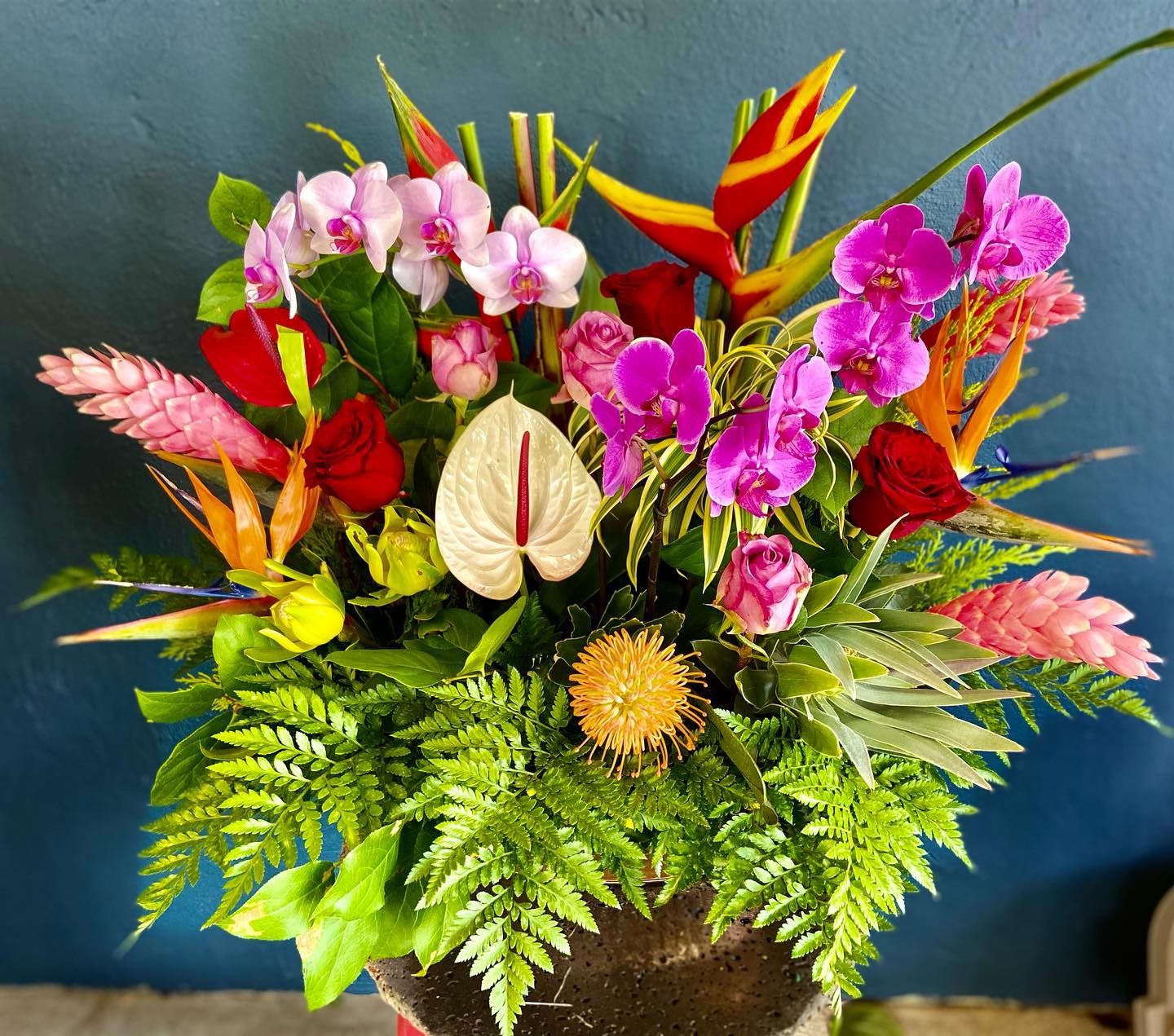 Large tropical arrangement with orchids, roses, anthurium, protea and birds of paradise in a dark pot
