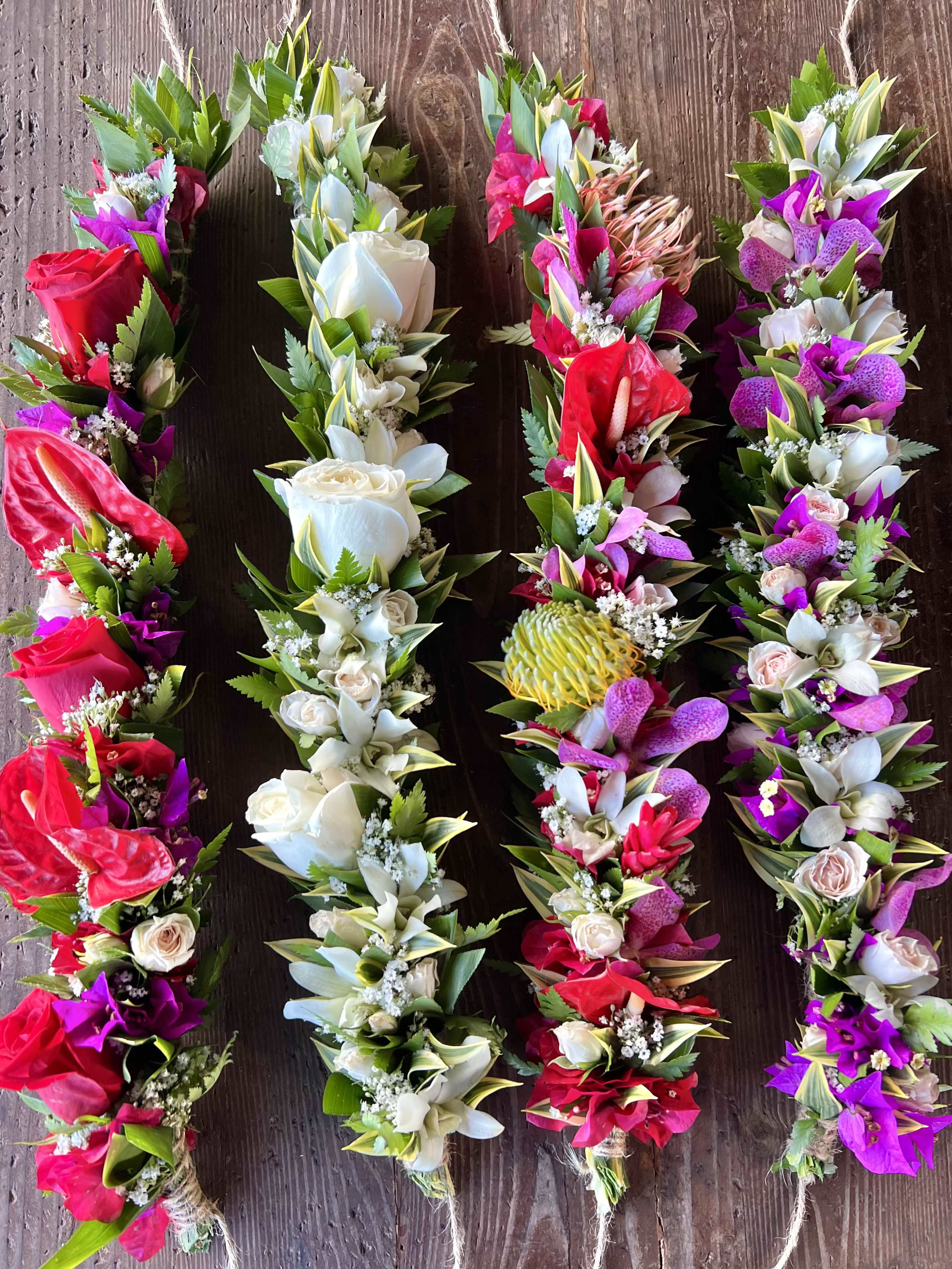 Set of four colorful floral garlands with red, white, pink, and purple blooms on a wooden surface