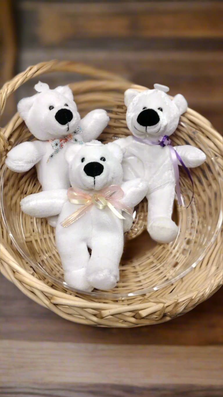 Three small white teddy bears with ribbons arranged in a wicker basket